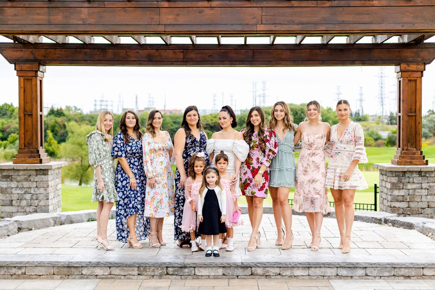 Group photo of people in floral dresses standing under a wooden pergola.