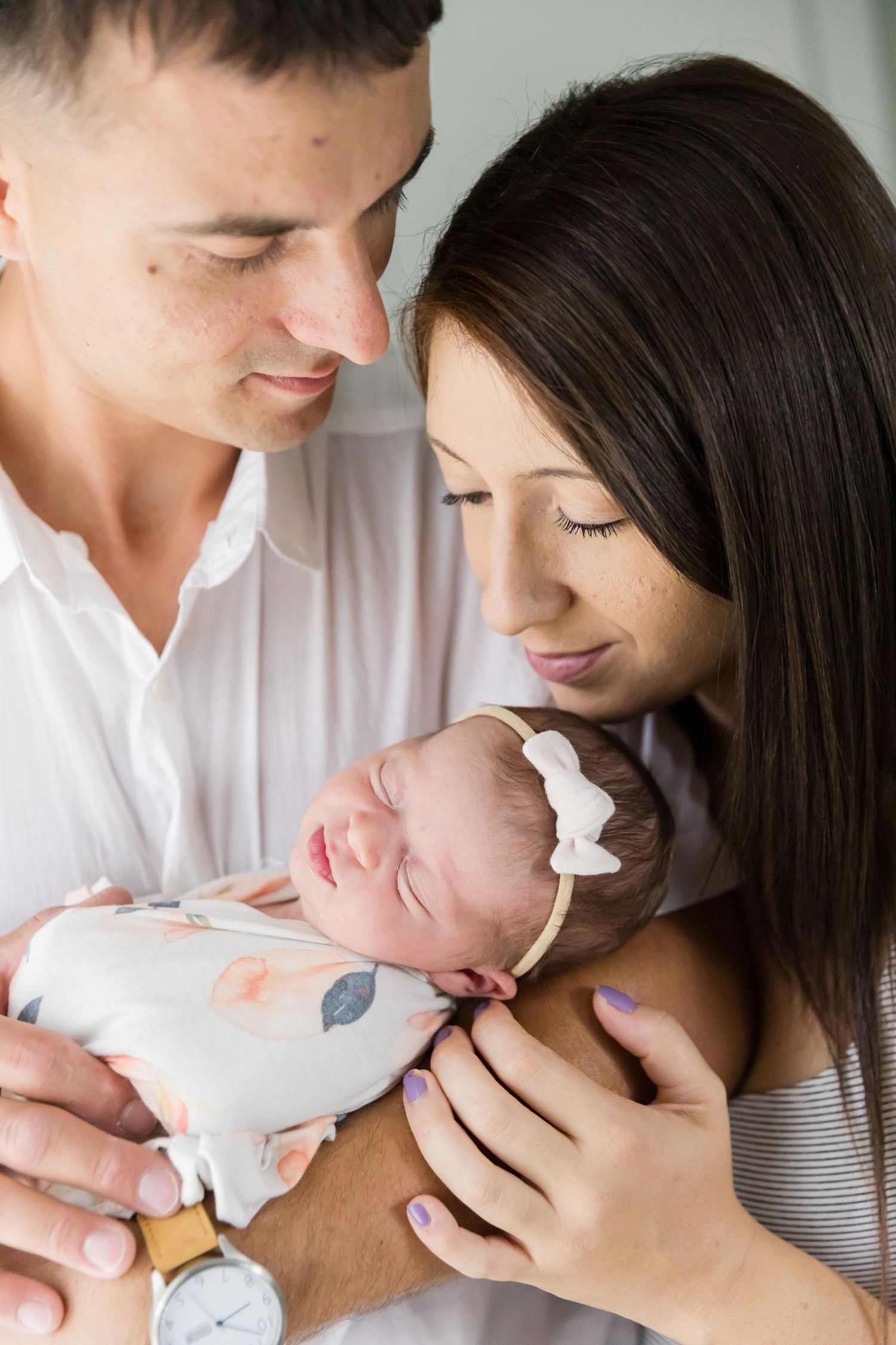 A couple gazes lovingly at their newborn baby wrapped in a floral swaddle blanket.