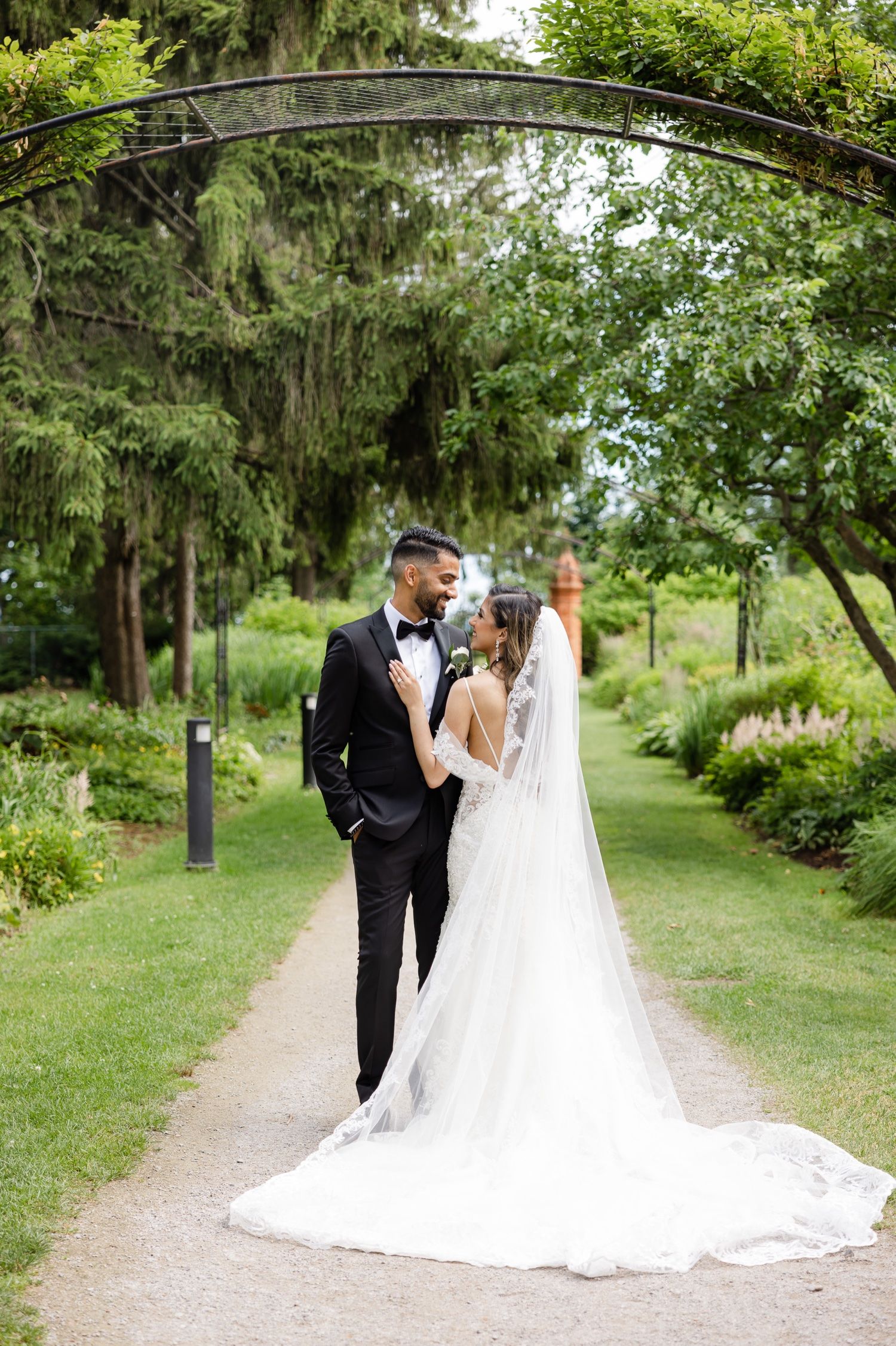A romantic wedding moment captured under a garden archway with flowing veil and greenery.