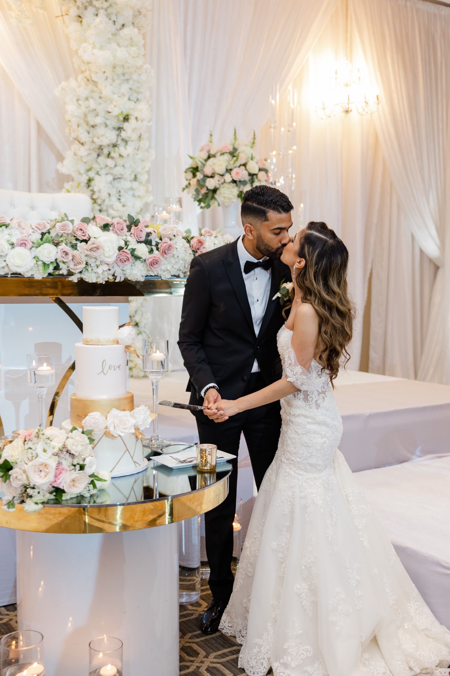 Newlyweds share an intimate moment beside their tiered wedding cake at an elegant reception.