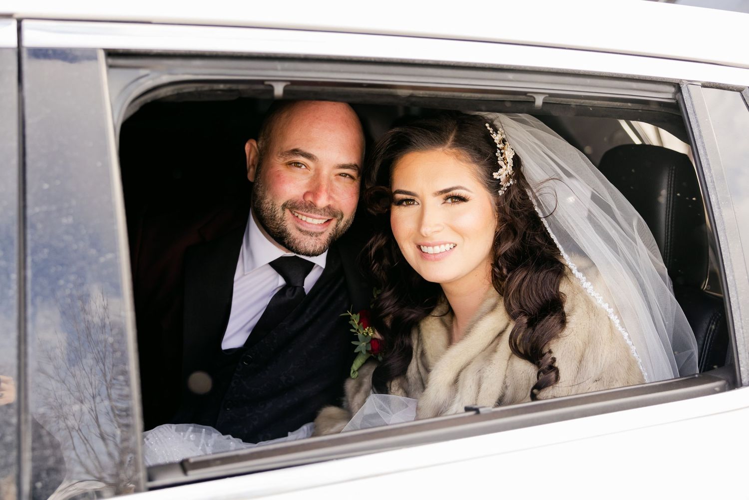 A romantic wedding car photo showing newlyweds smiling through the window of their vehicle.