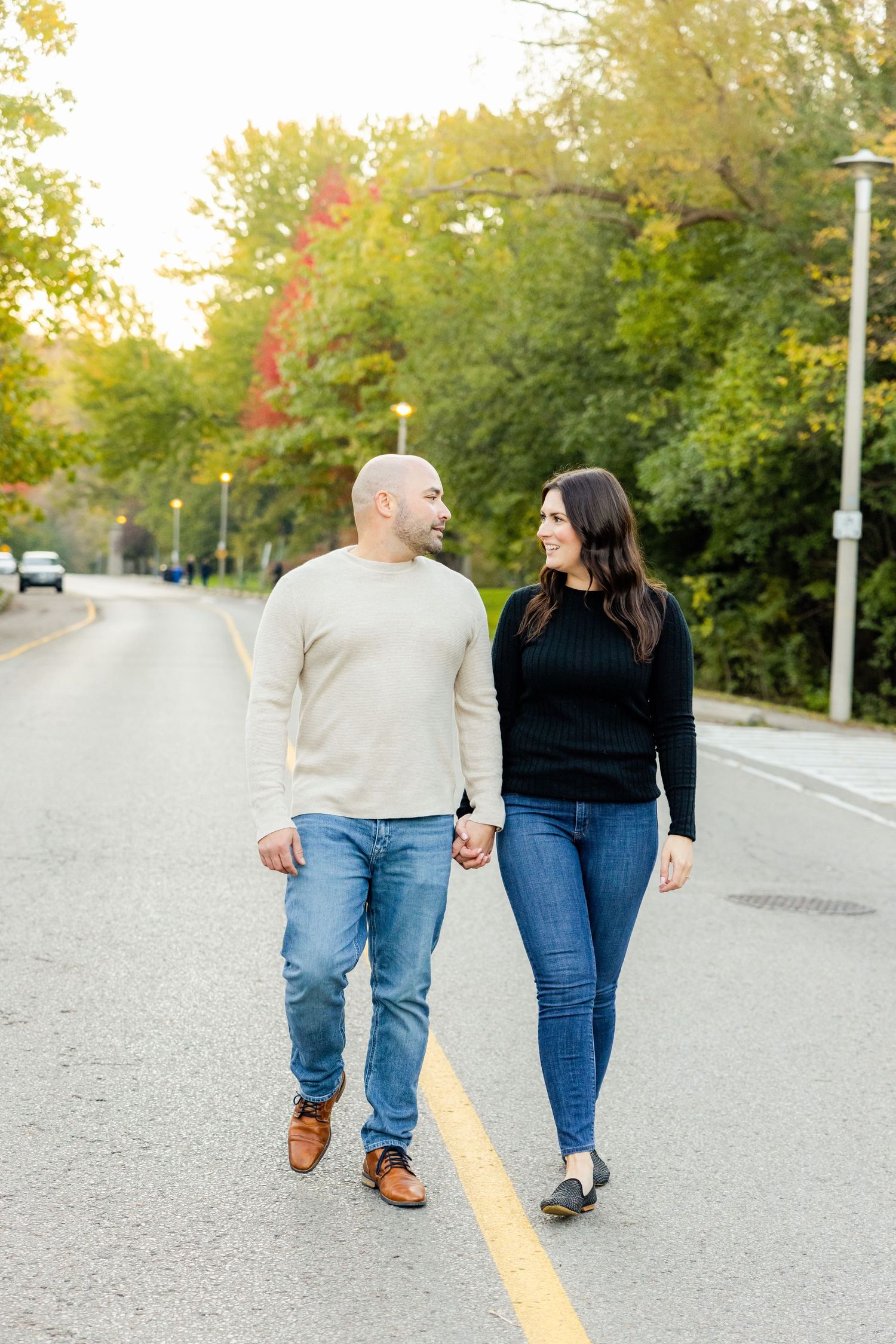 A couple walks together holding hands on a tree-lined street during golden hour in autumn.