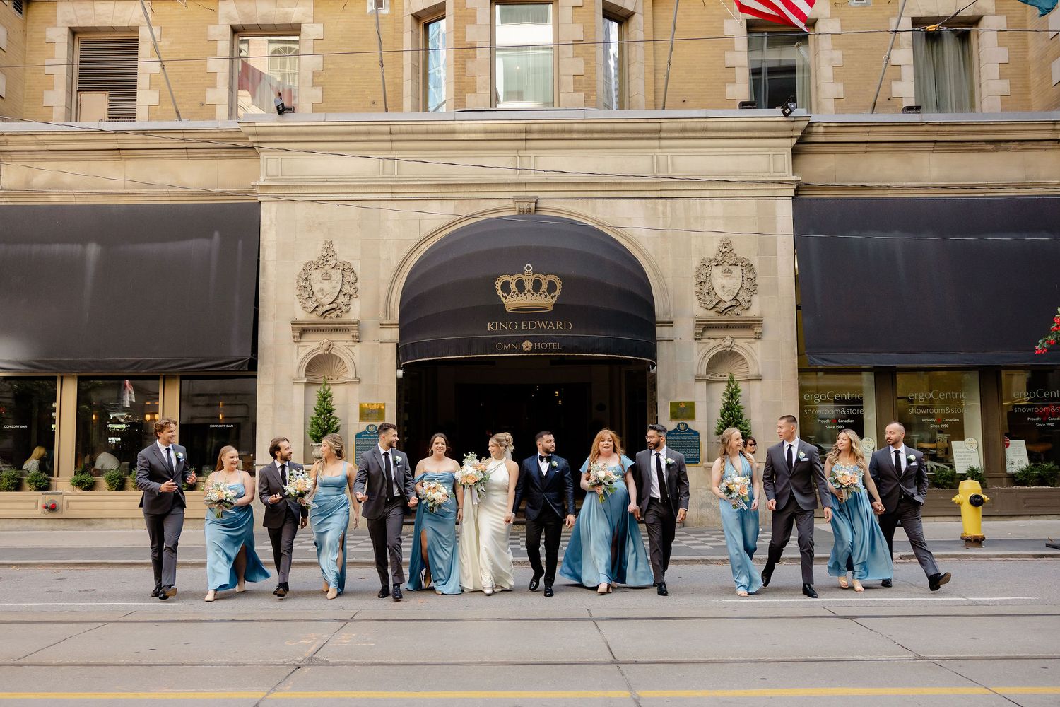Wedding party members arranged in front of a grand hotel entrance with American flag.