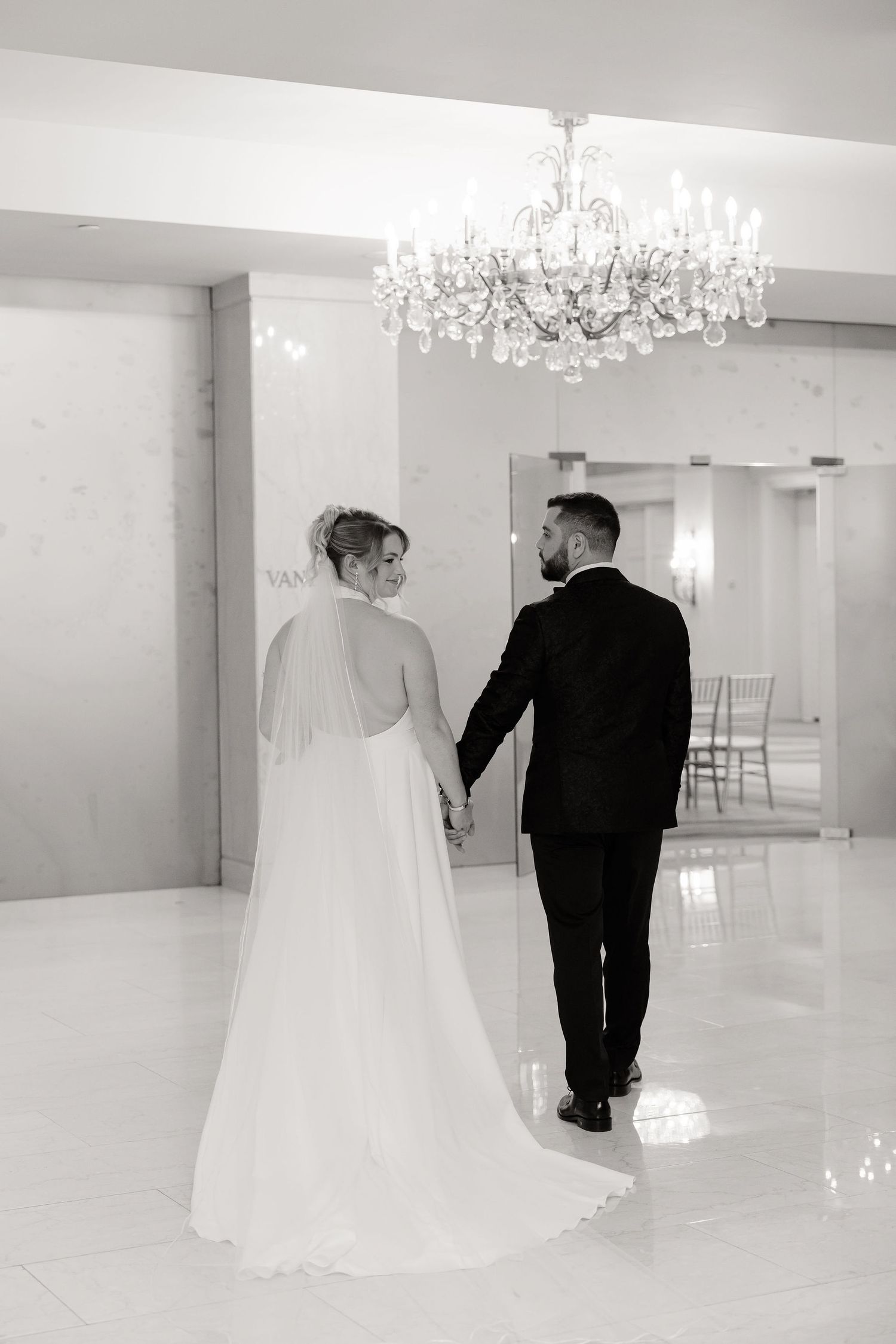 Black and white wedding photos showing couple walking across elegant ballroom with chandeliers.