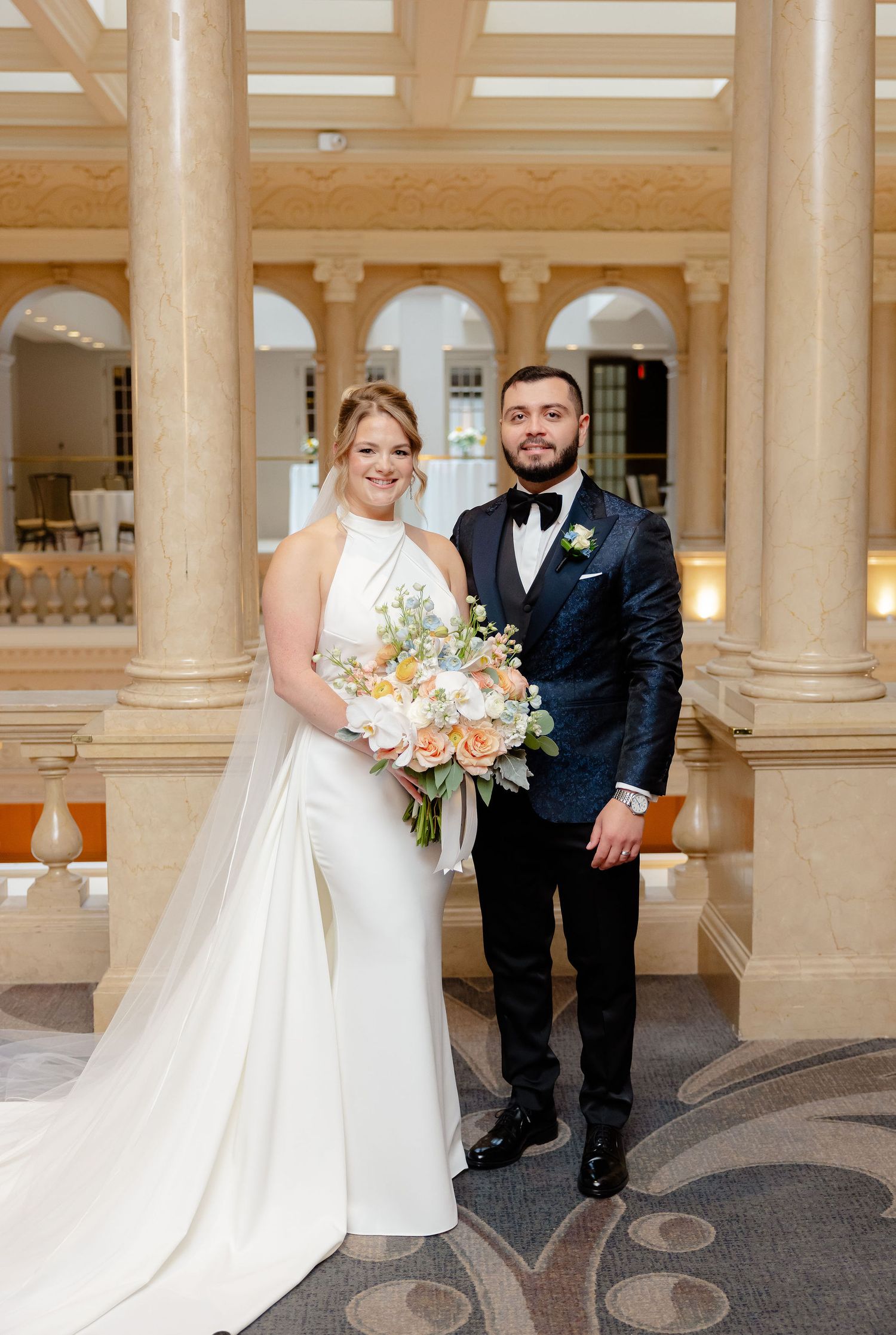 A bride and groom share intimate moments in an elegant columned hallway with marble floors during their wedding.