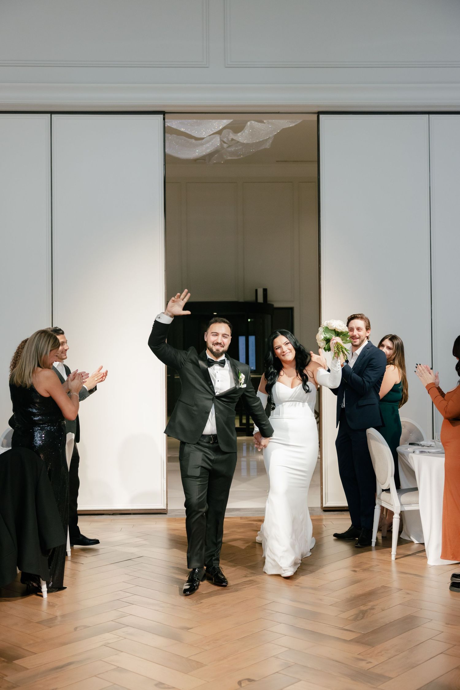 Newlyweds celebrate their entrance at reception with guests cheering.