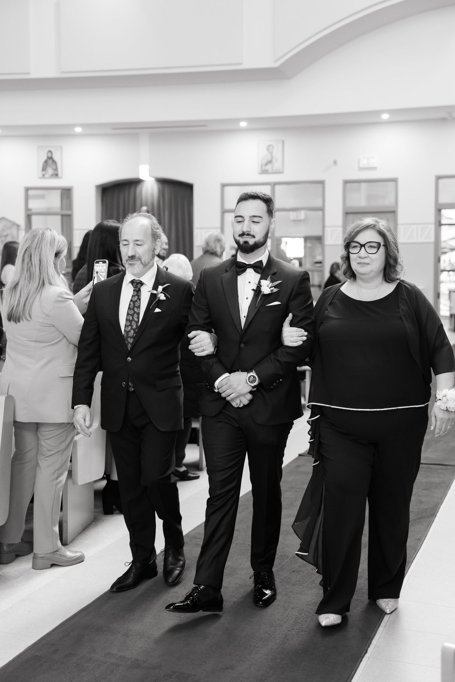 Black and white photo of wedding party members walking down church aisle together.