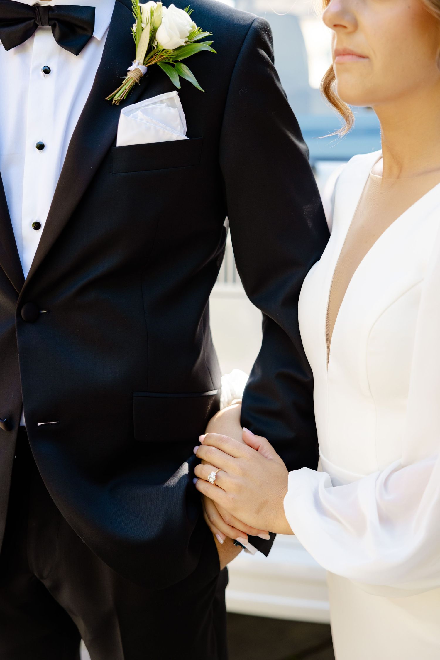 Detail shot of wedding attire showing black tuxedo with boutonniere next to white dress sleeve.