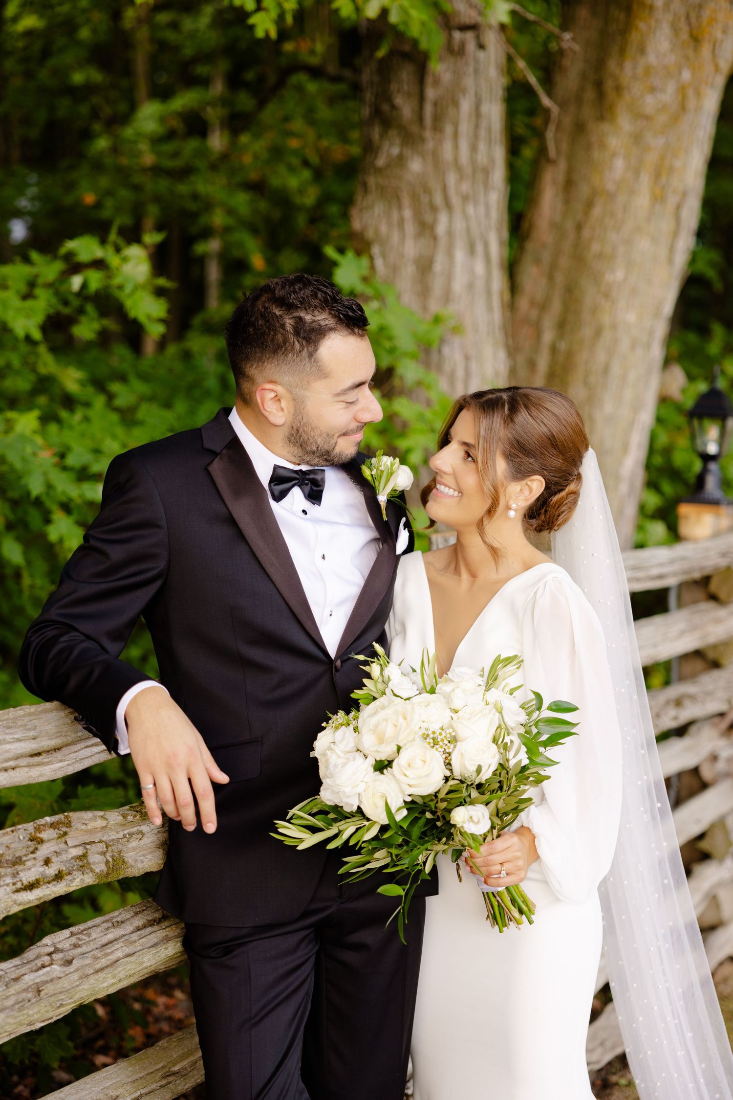 An intimate wedding moment captured by a rustic fence with the couple in formal attire.
