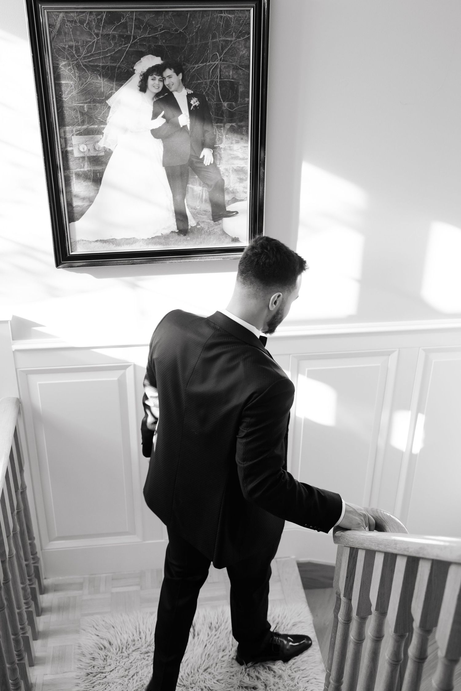 A black and white photo shows someone ascending stairs beside a framed vintage wedding photograph.