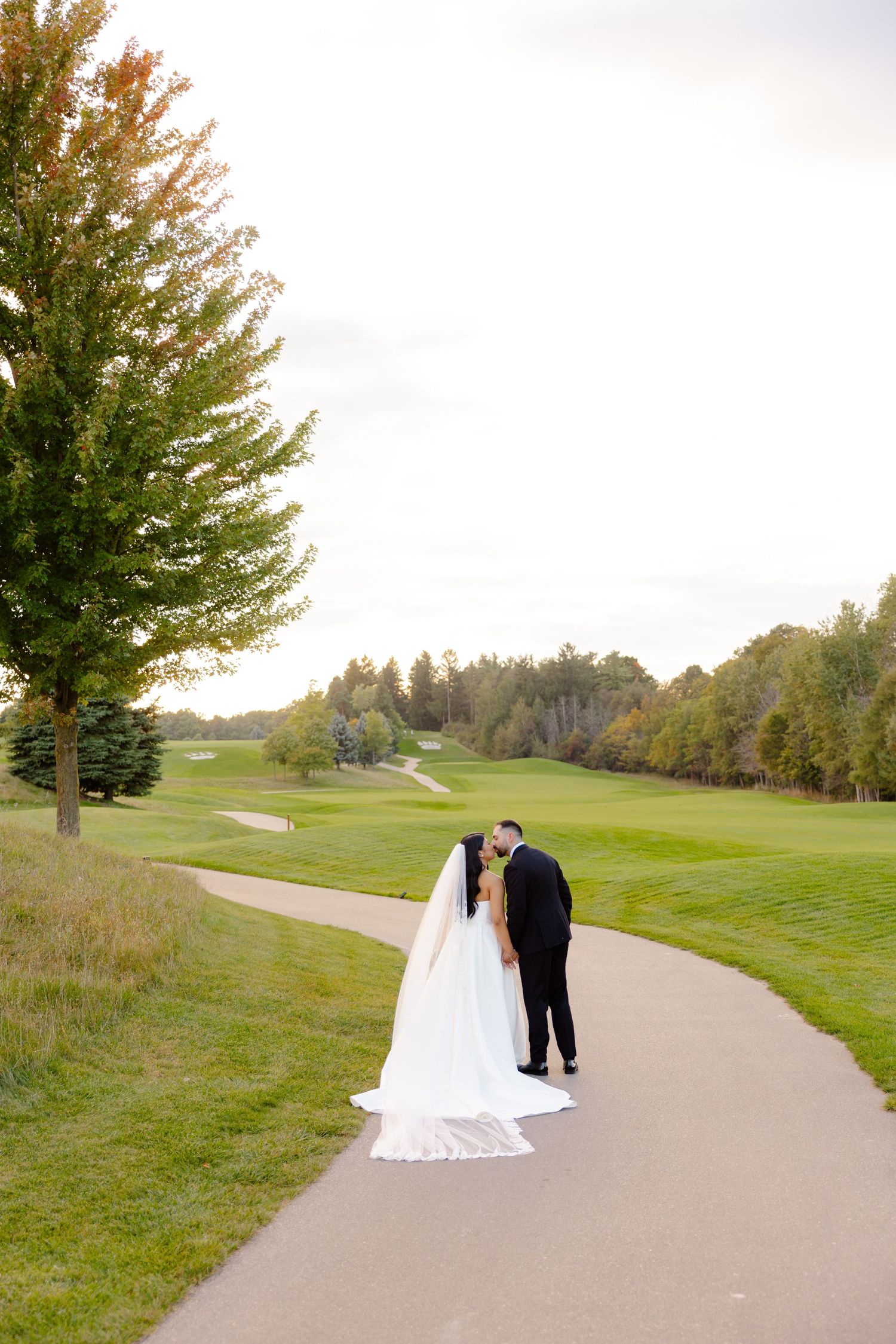 A couple shares a moment on a winding golf course path surrounded by autumn trees.