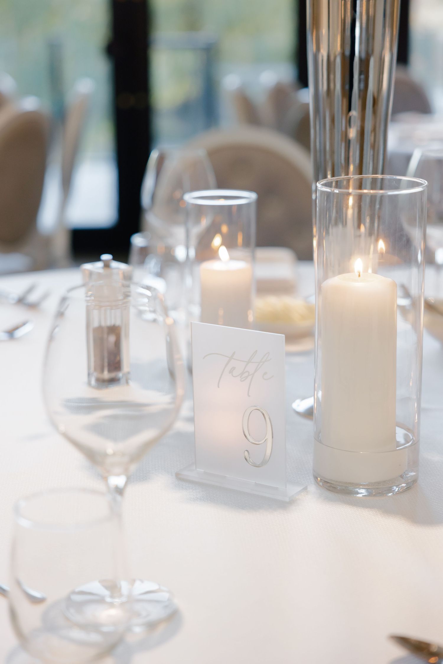 Close-up of wedding table decor with table number 9, white candles in glass holders and wine glasses.