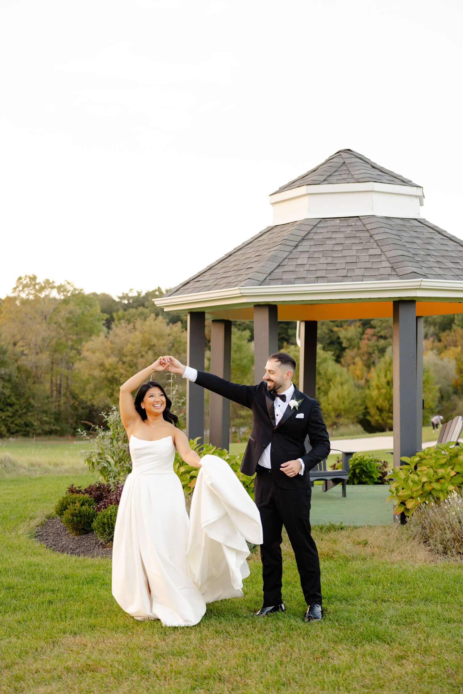 A playful wedding couple dances and twirls by their garden gazebo.