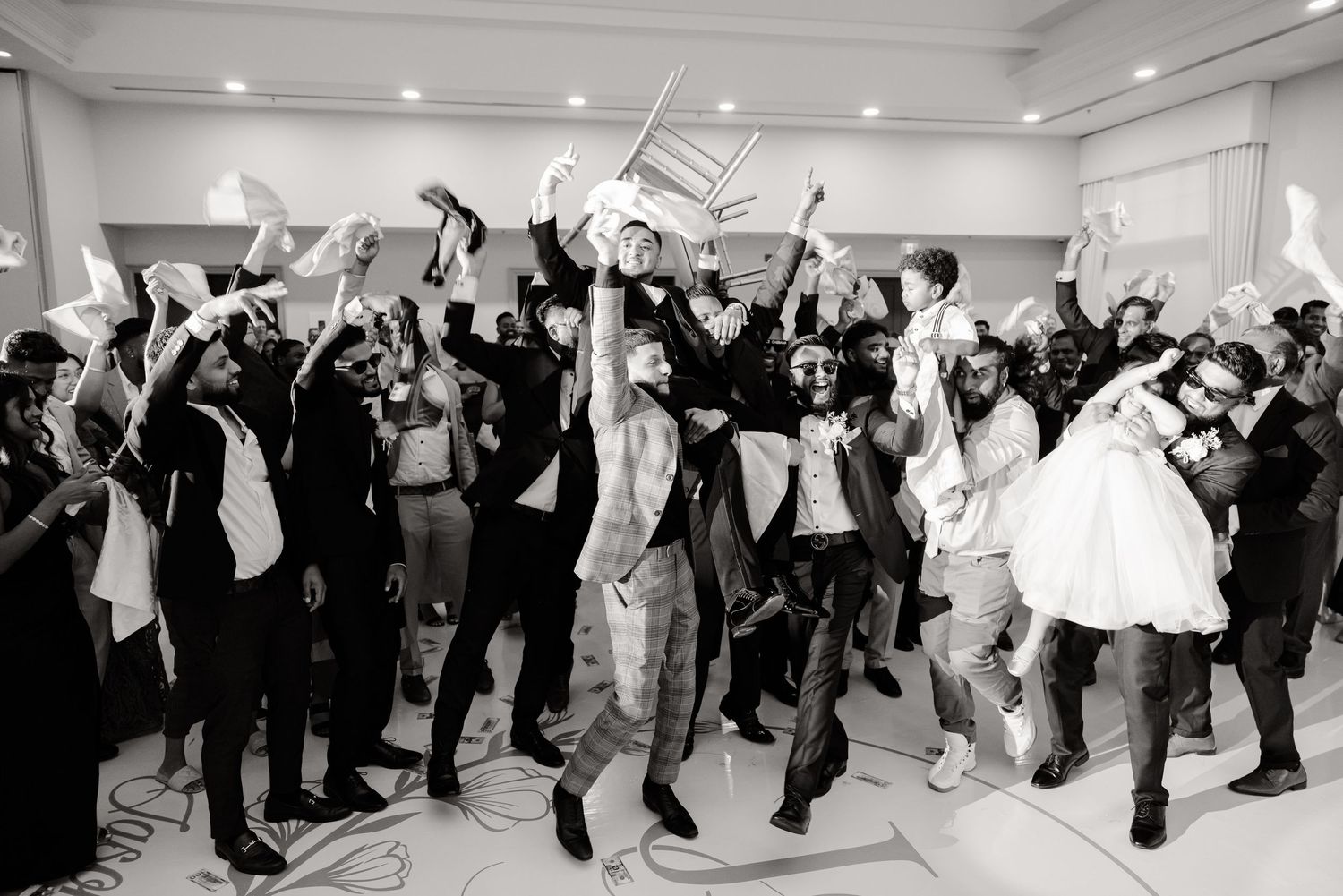 Black and white photo of wedding guests jumping and dancing with joy during reception celebration.