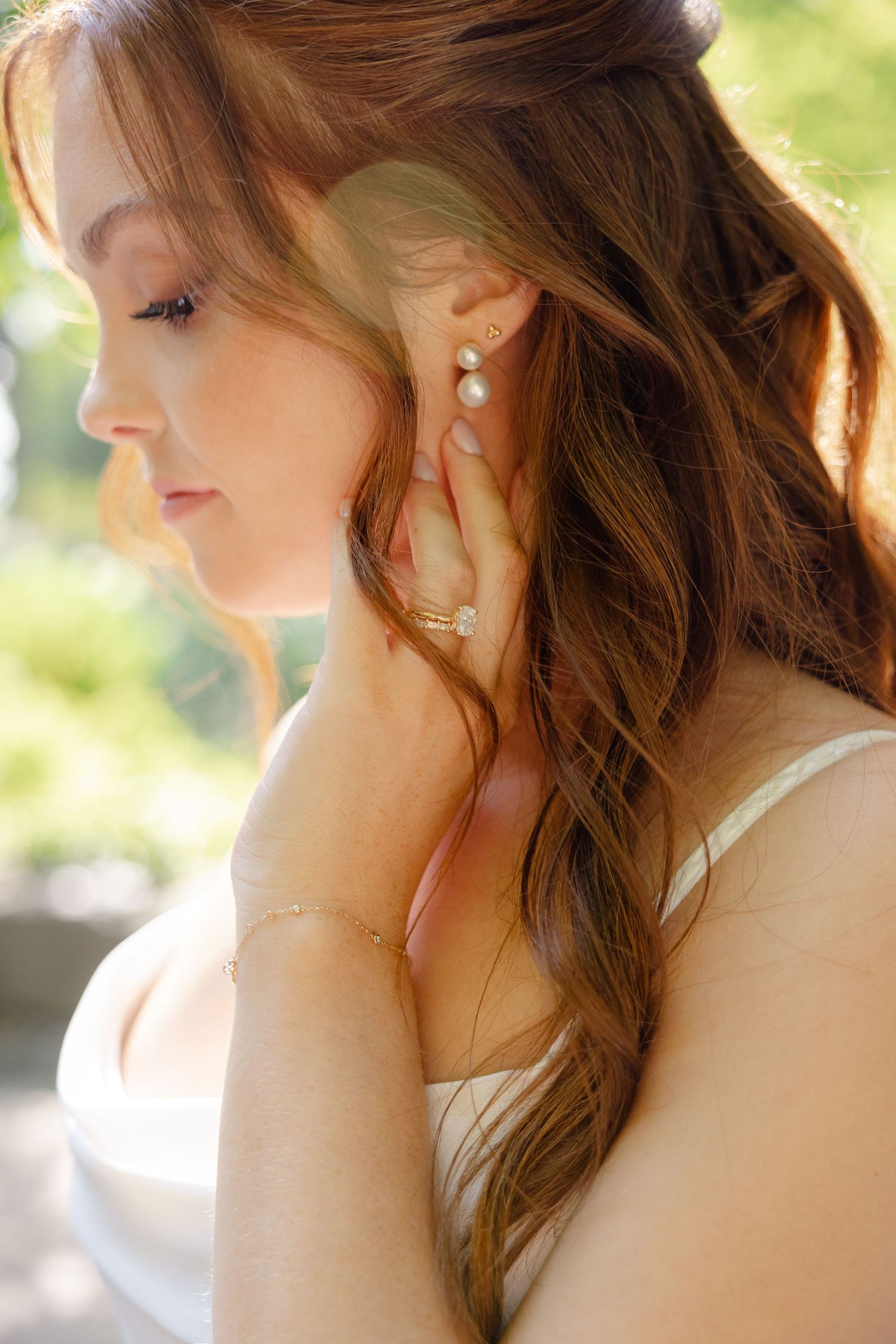 Close-up profile view of bridal jewelry and soft romantic hairstyling against a sunlit natural backdrop.