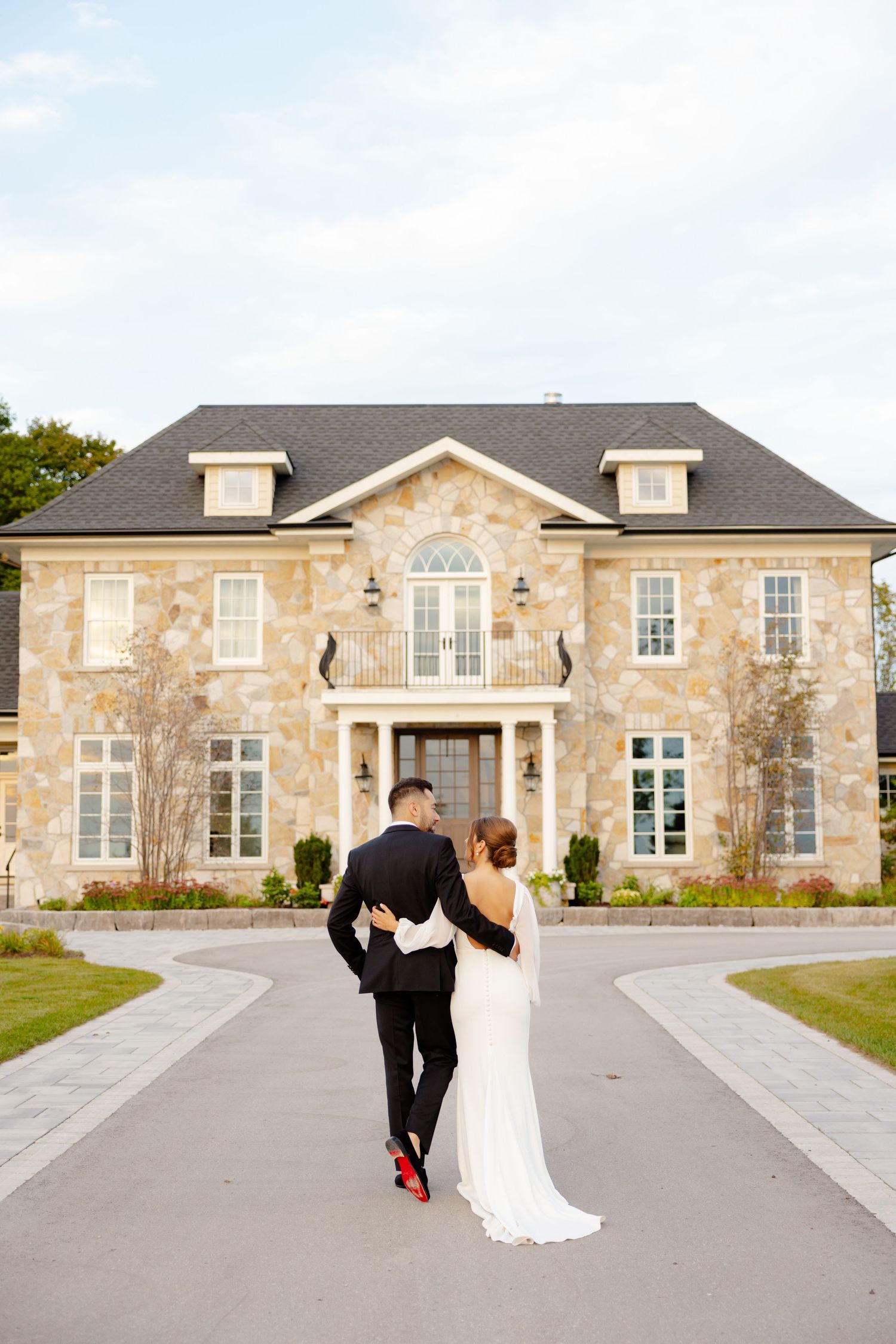A couple walking towards an elegant stone mansion on their wedding day.