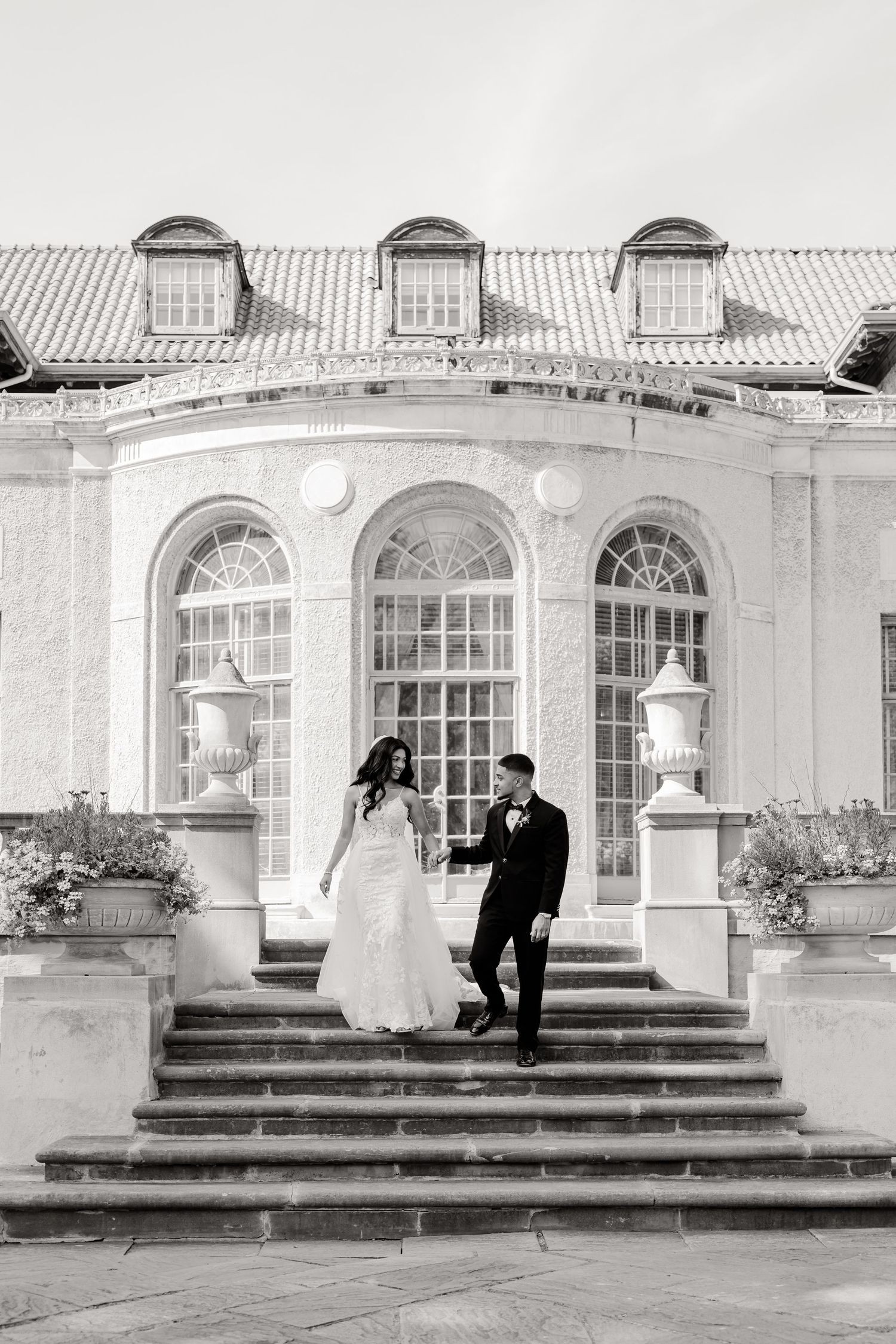 Black and white wedding photo on grand steps of a classical building with three arched windows.