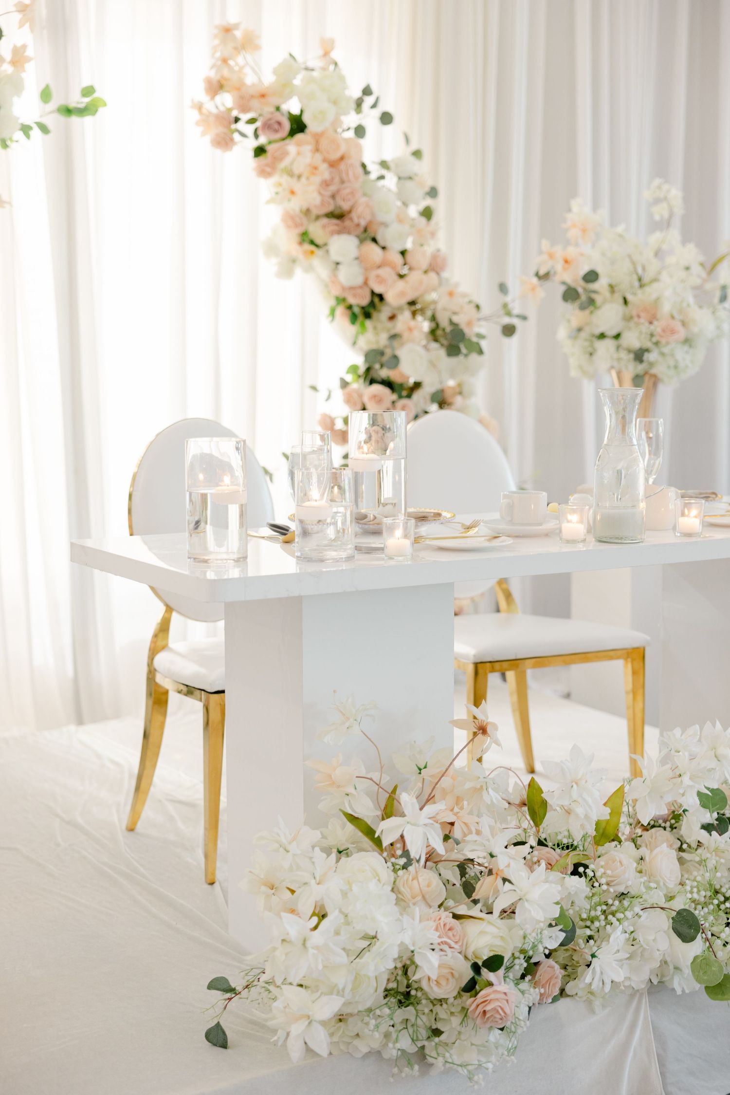 Romantic sweetheart table setup with white and blush floral arrangements and gold accents.