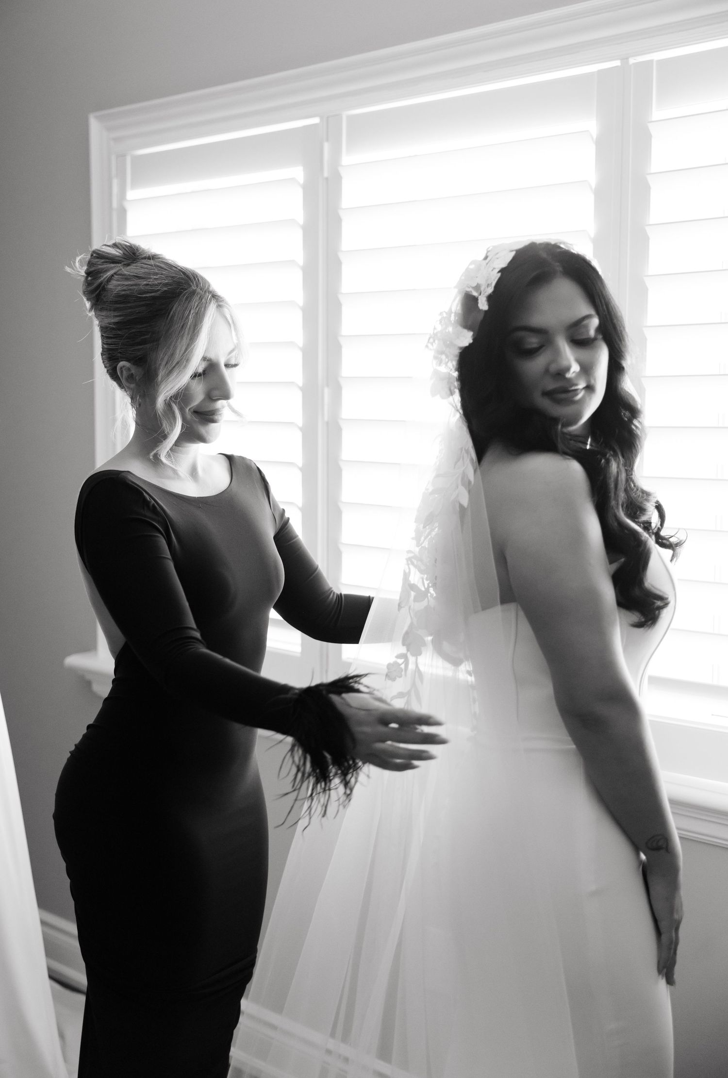 Black and white photo of bridal preparation with stylist helping adjust the wedding dress.