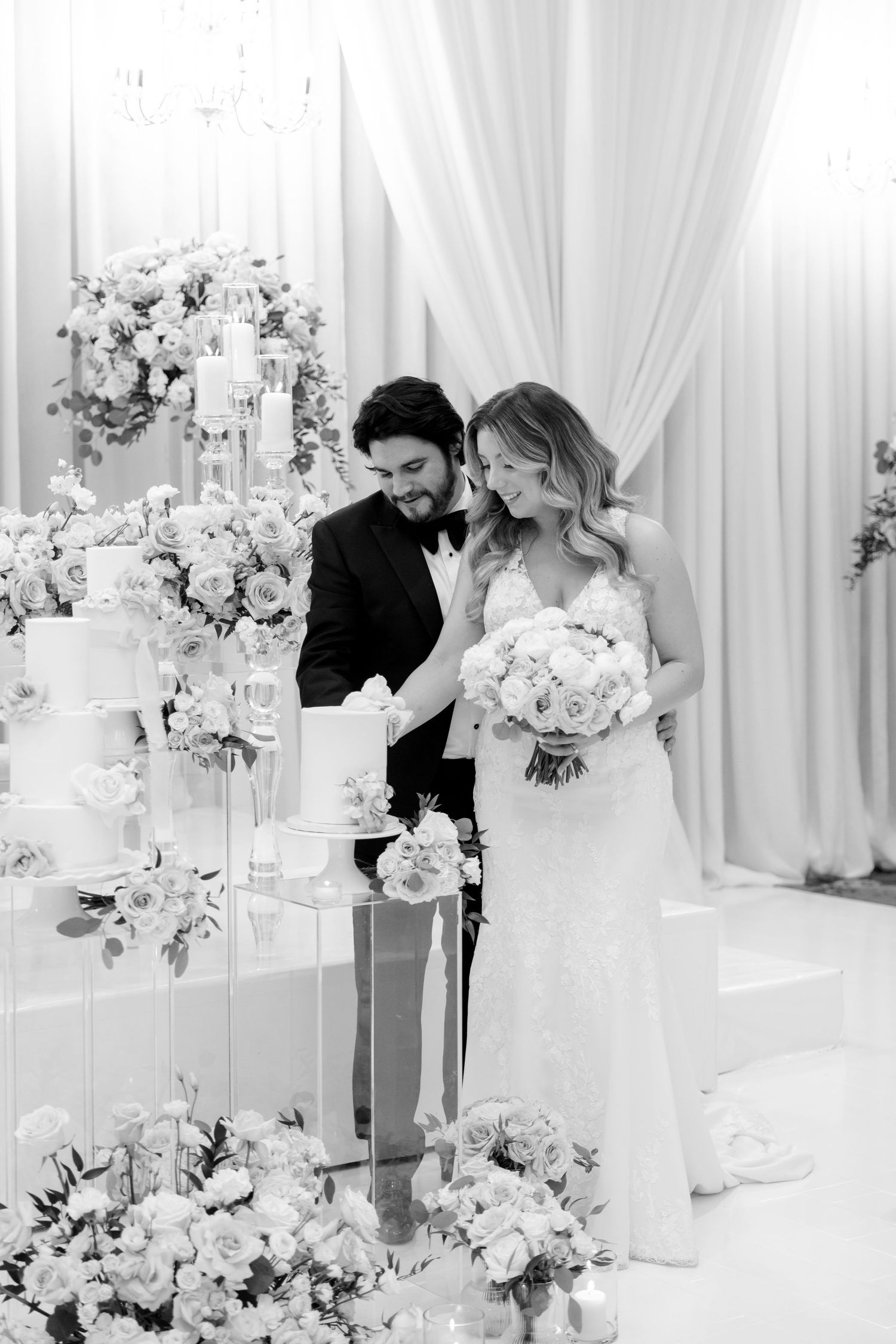 Black and white wedding photo with elegant cake display and floral arrangements.