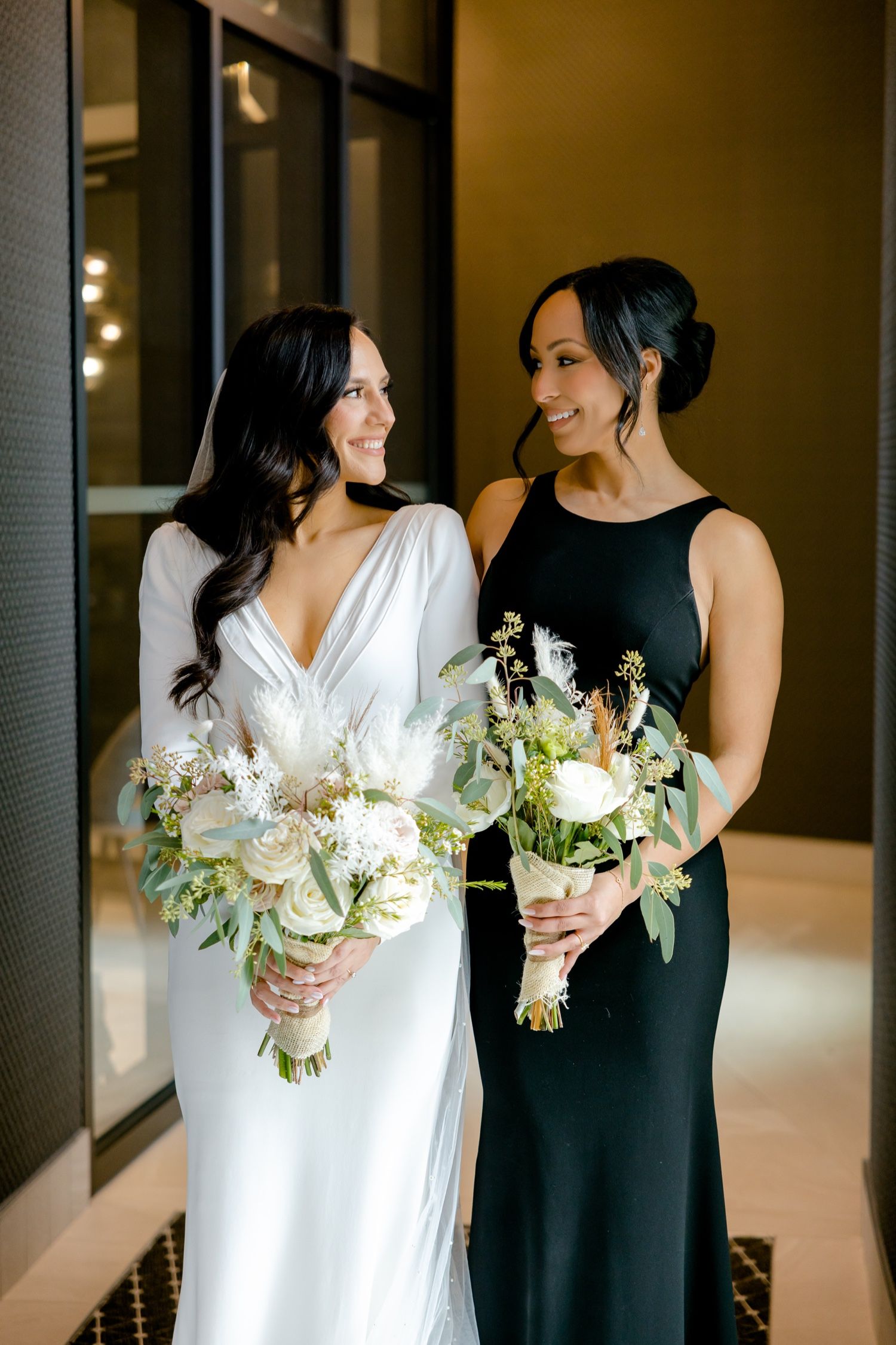 Wedding portrait of two women holding white floral bouquets in elegant black and white attire.