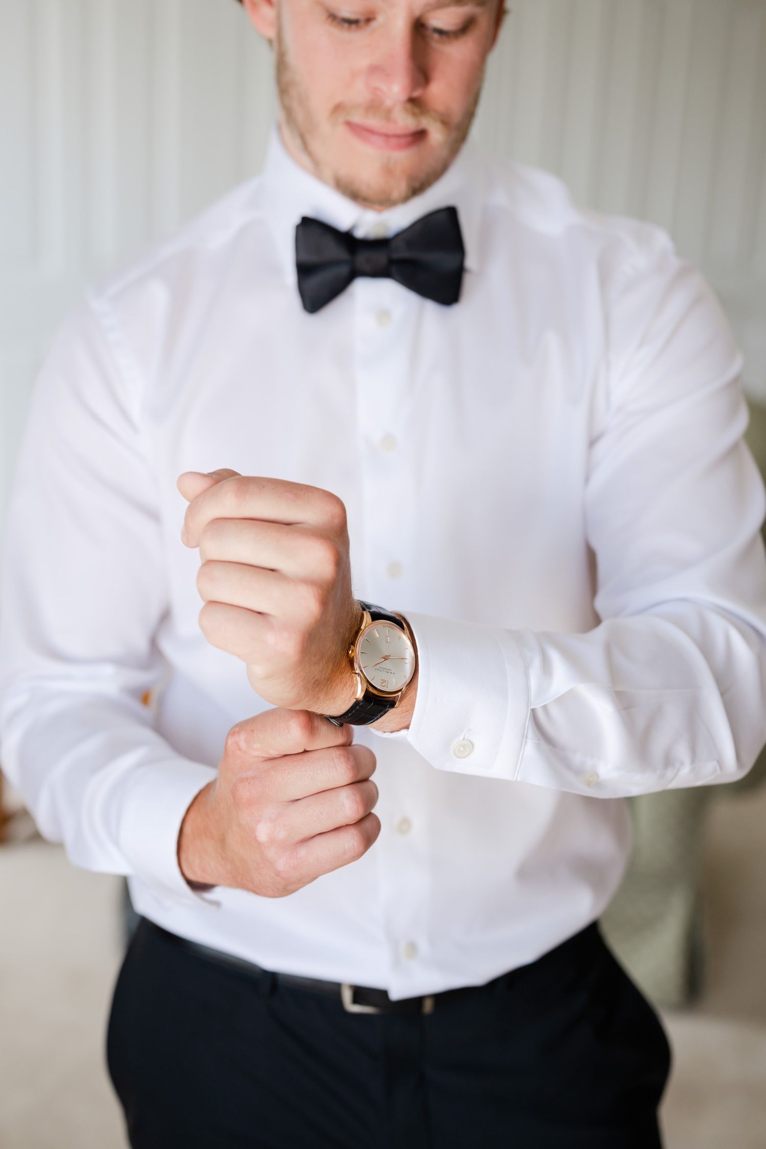 Close-up of a person in a white dress shirt and black bowtie adjusting their wristwatch.