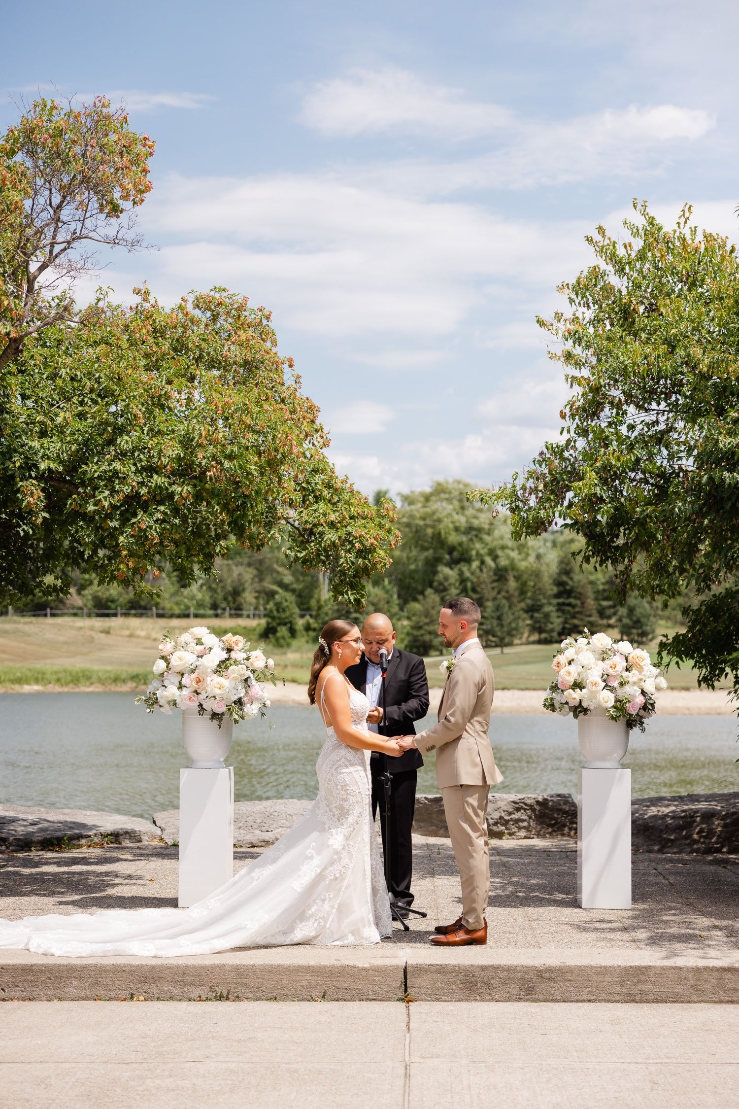 Intimate lakeside wedding ceremony with white floral columns and natural landscape.