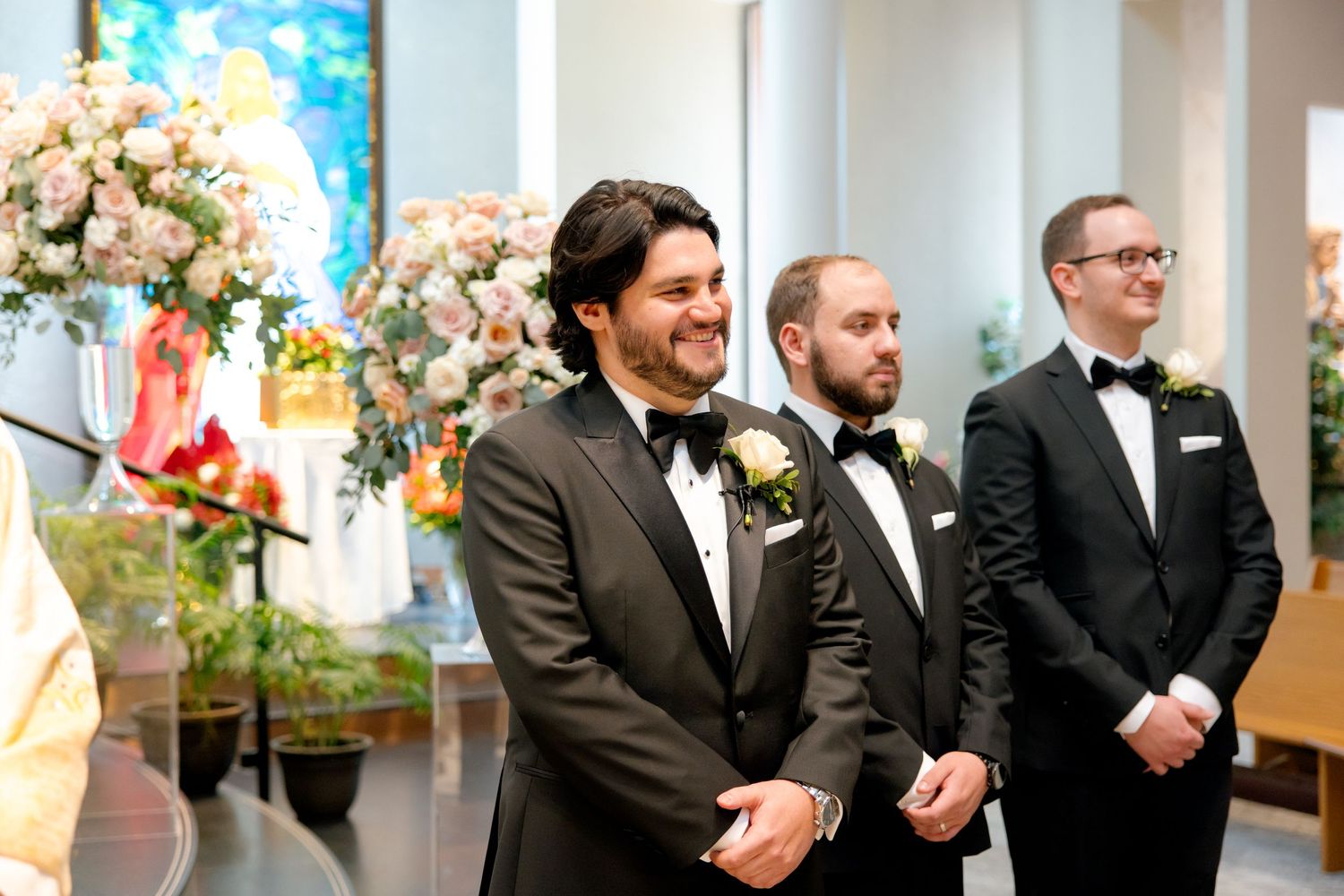 Wedding ceremony with elegant floral arrangements and suited groomsmen at altar.