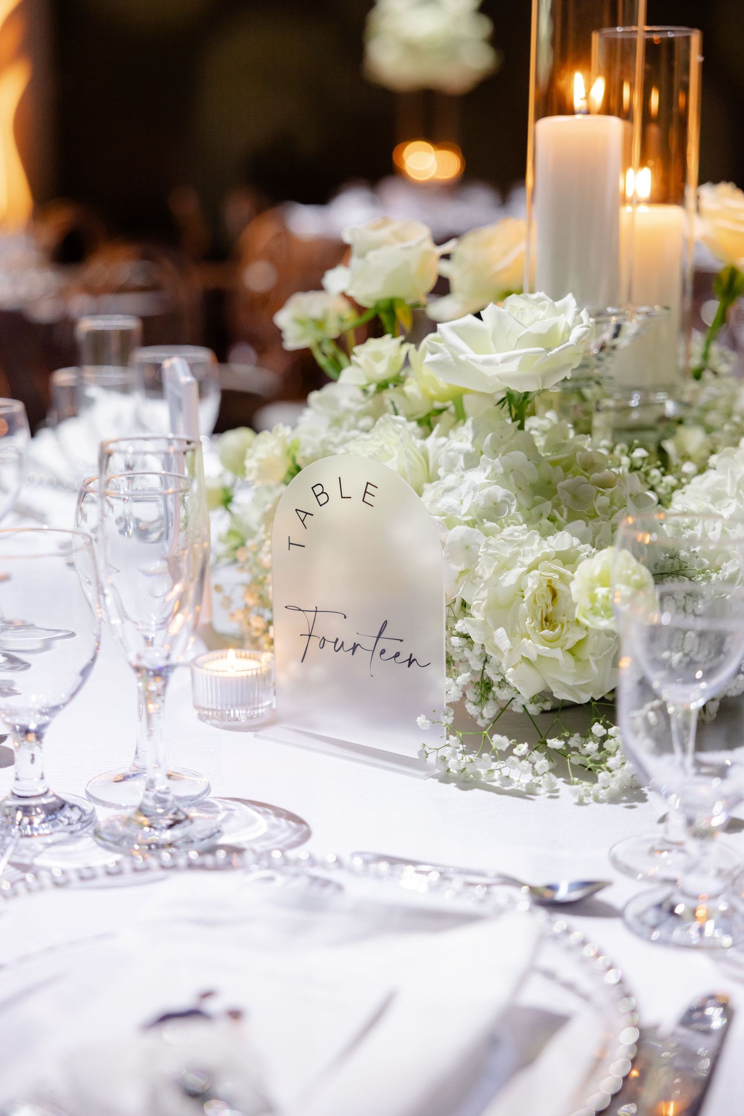 Elegant wedding table setting with white floral centerpiece, glowing candles, and table number card.