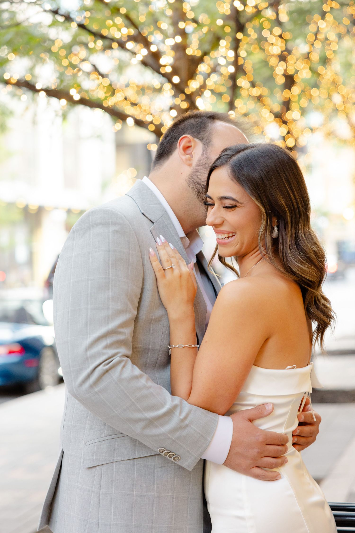 Romantic embrace on city street with fairy lights twinkling in trees.
