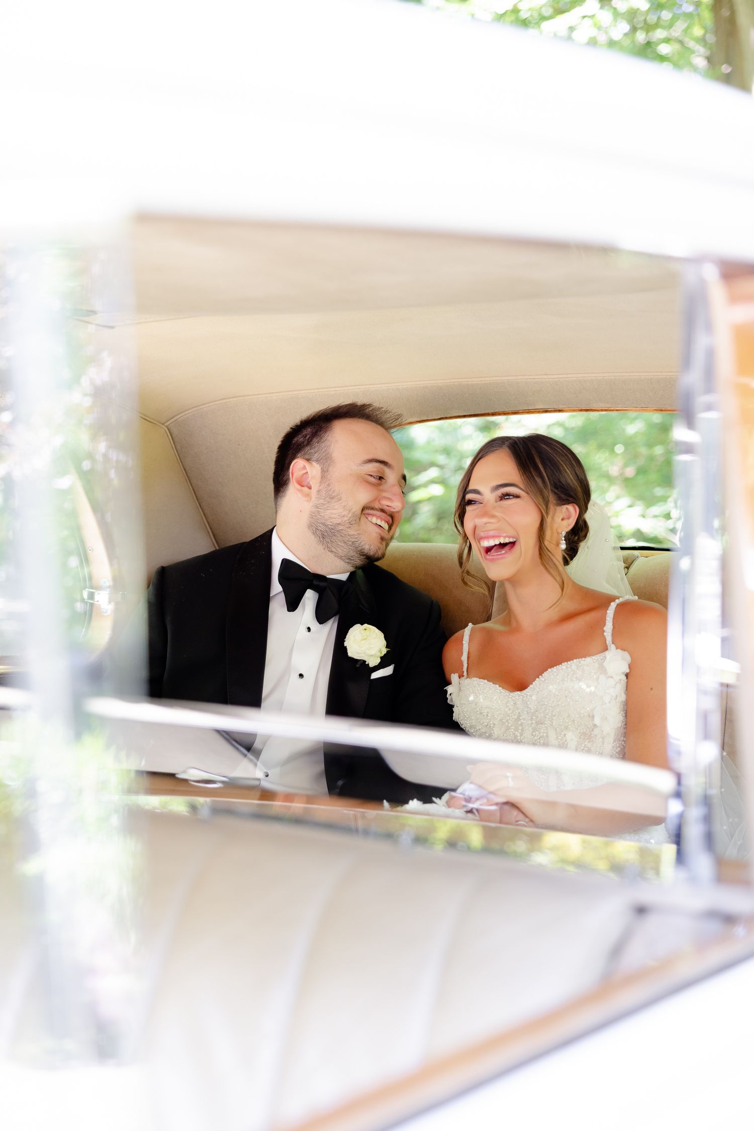 A joyful candid moment of a bride and groom laughing together in the back of their wedding car.