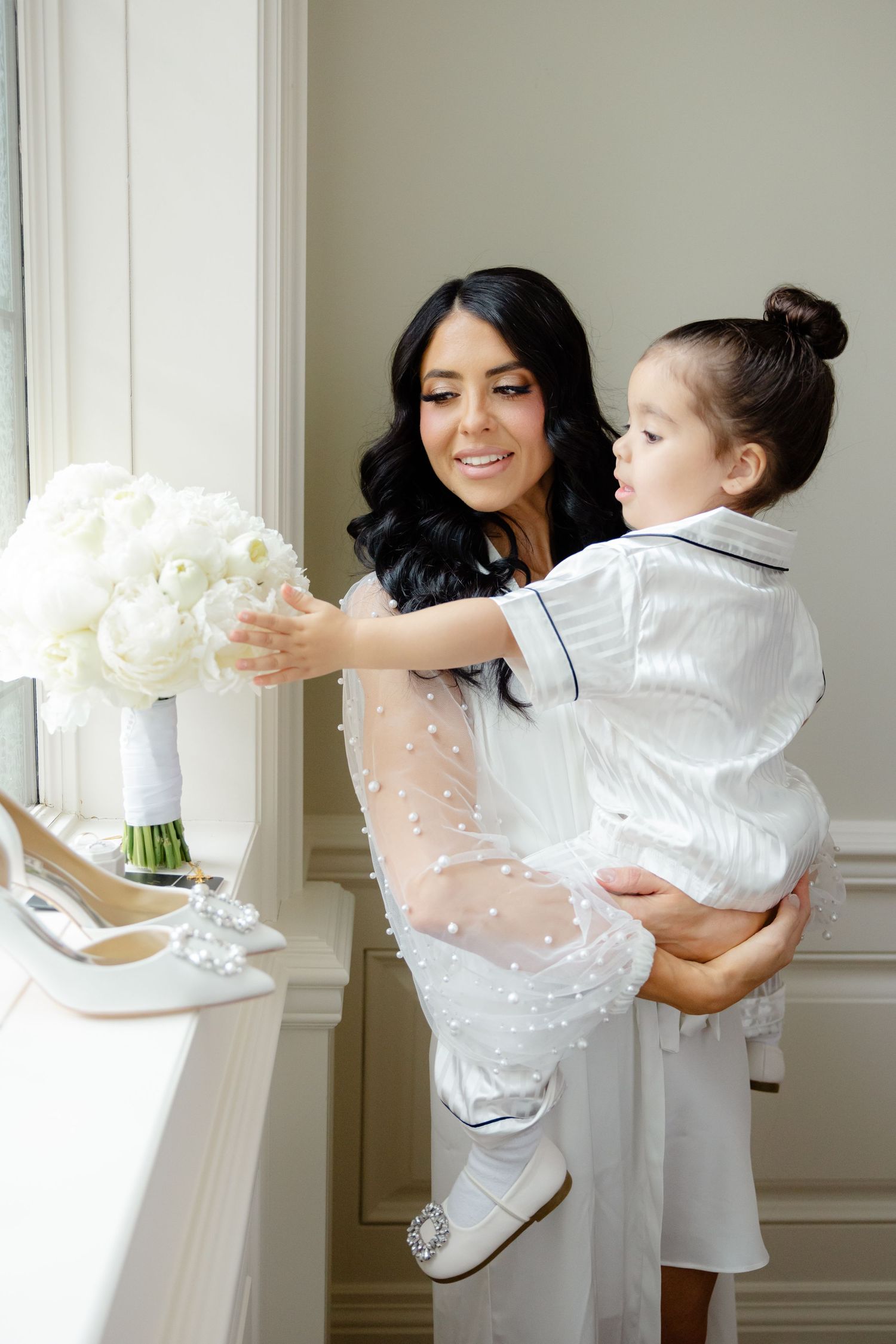 A tender moment between parent and child as they admire a white floral bouquet by a window.