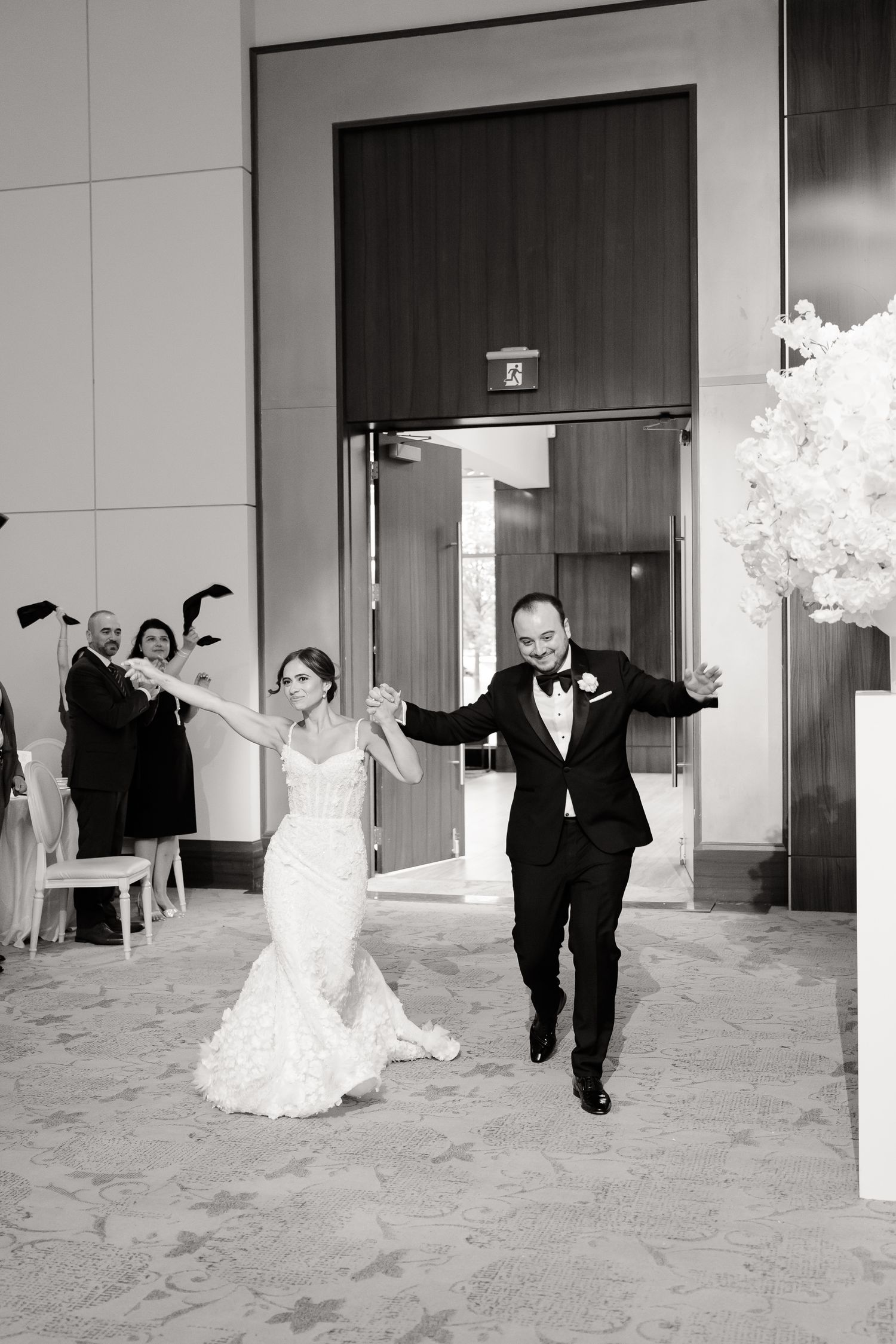 A jubilant newlywed couple makes their grand entrance at a wedding reception in black and white photography.