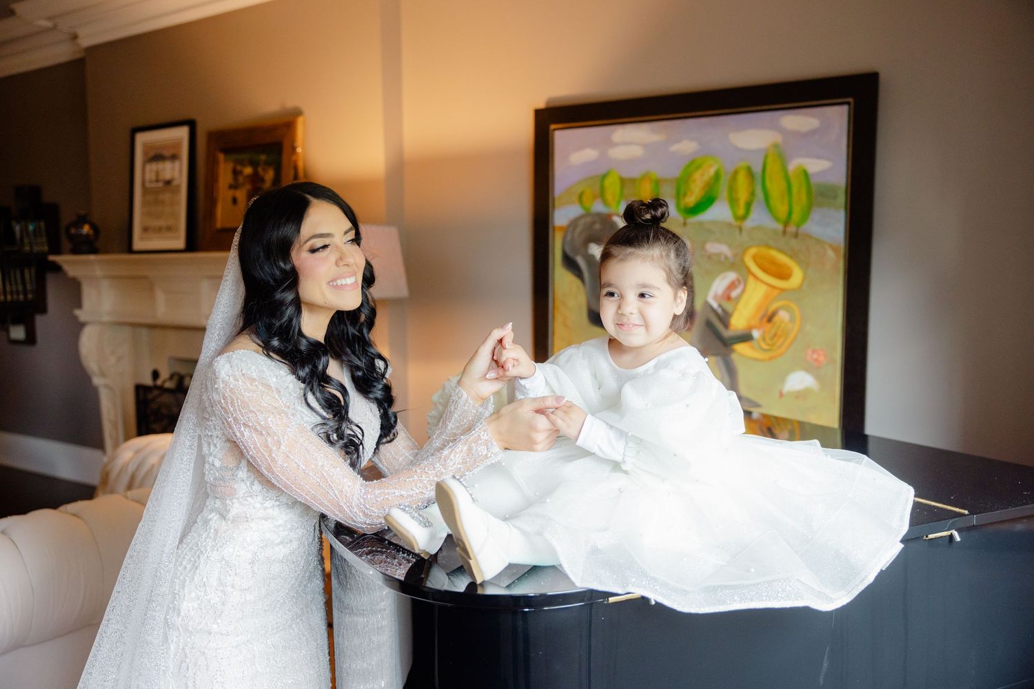 A bride in lace gown helps a young attendant balance on a grand piano.