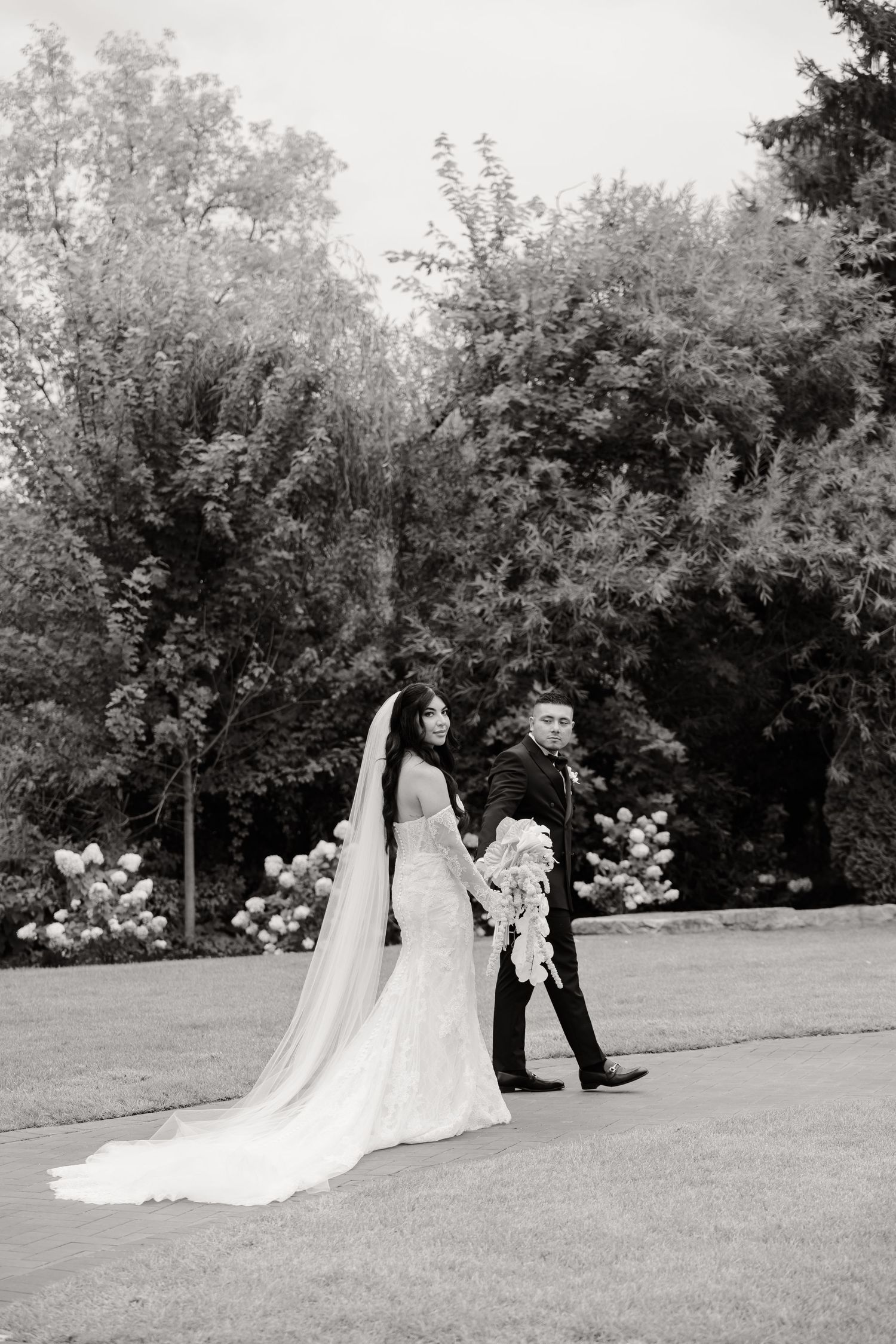 A sequence of black and white wedding photos showing a couple posing on a scenic lawn with trees and flowers in the background.