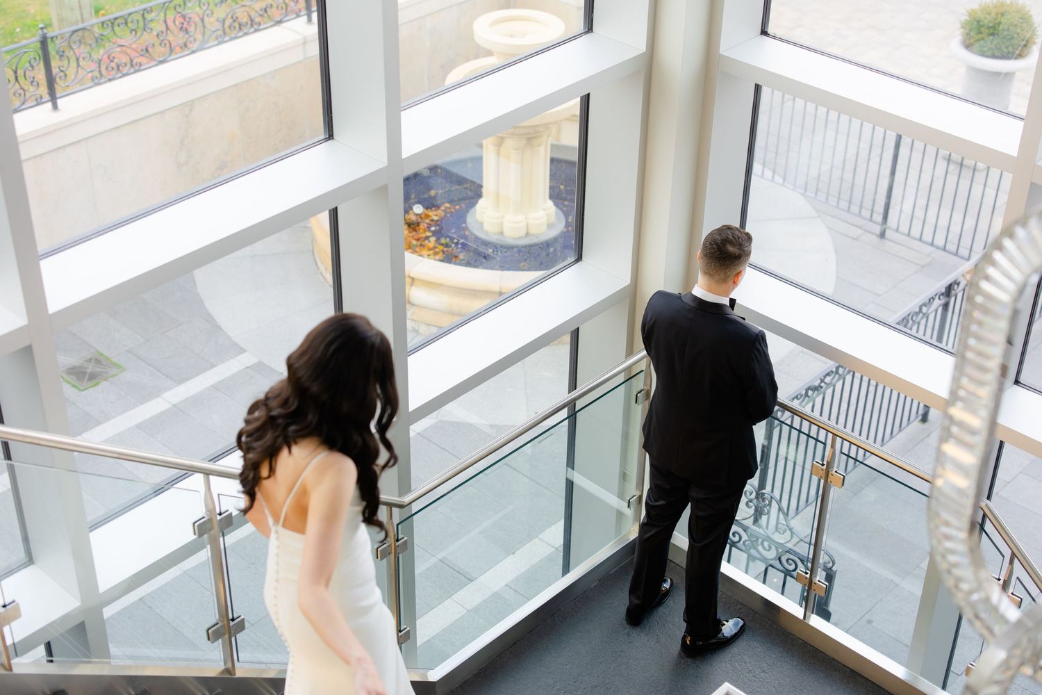A wedding couple stands apart during their first look moment in a modern stairwell.
