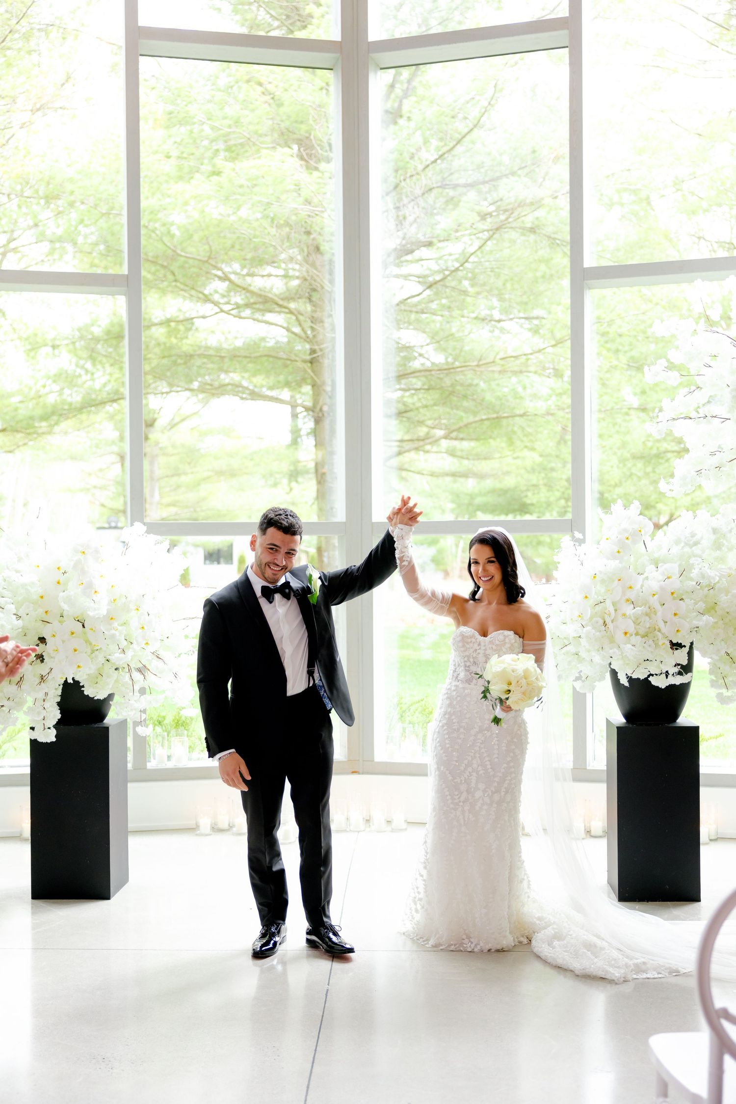 A romantic wedding scene with a couple celebrating in front of floor-to-ceiling windows and floral arrangements.
