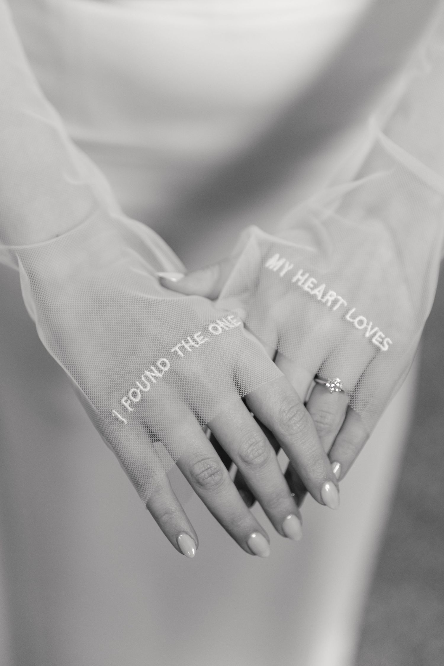 Close-up black and white photograph of hands wearing an engagement ring with round diamond solitaire.