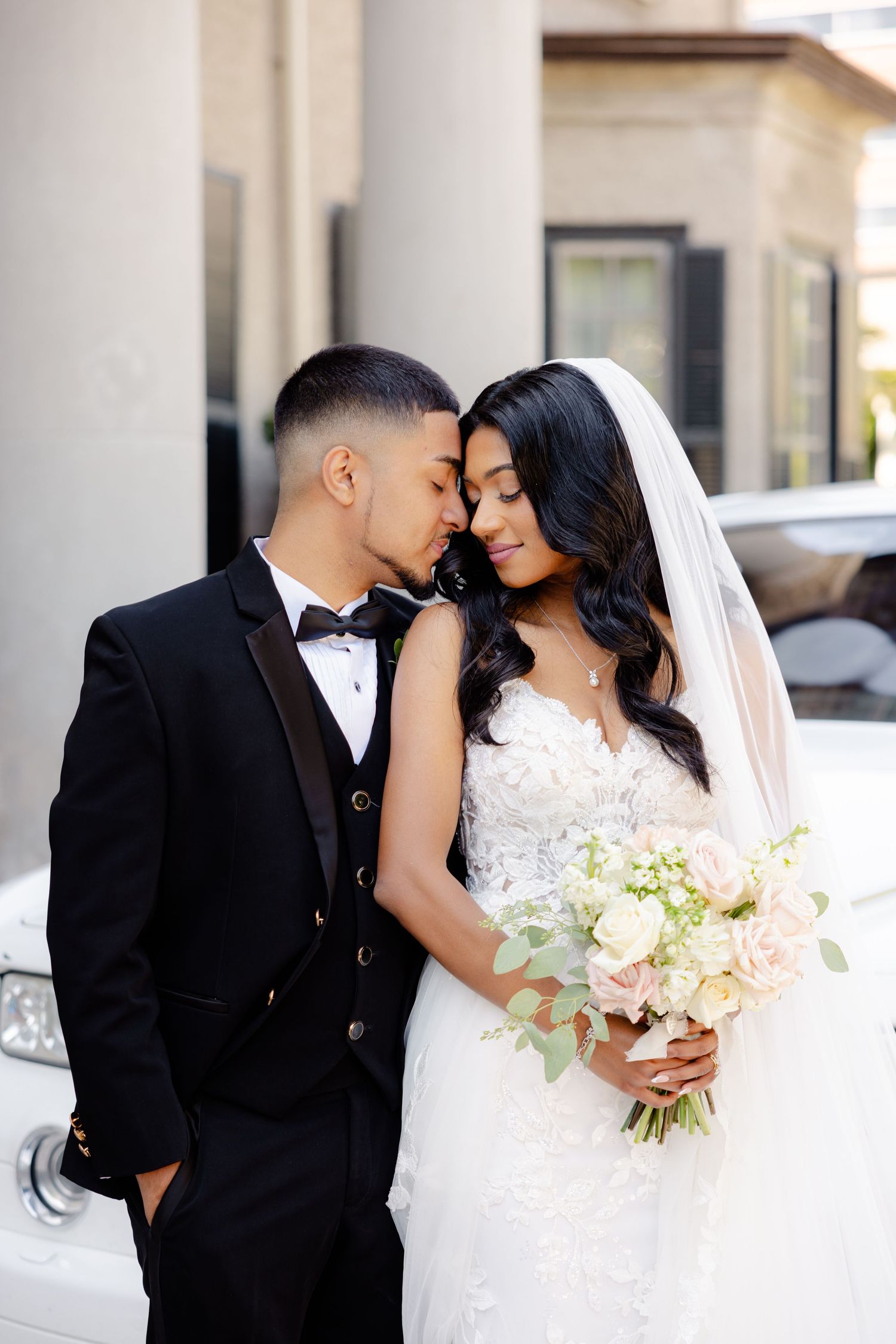 Intimate wedding portrait with couple sharing tender moment beside luxury car.