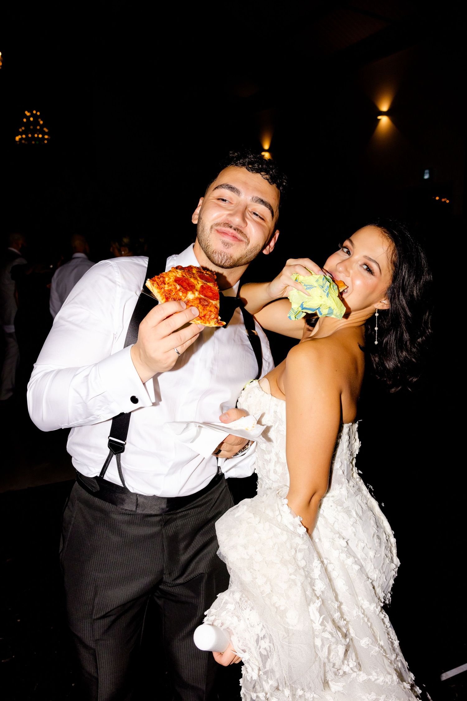 Wedding couple playfully eating and posing with their late night reception snacks.