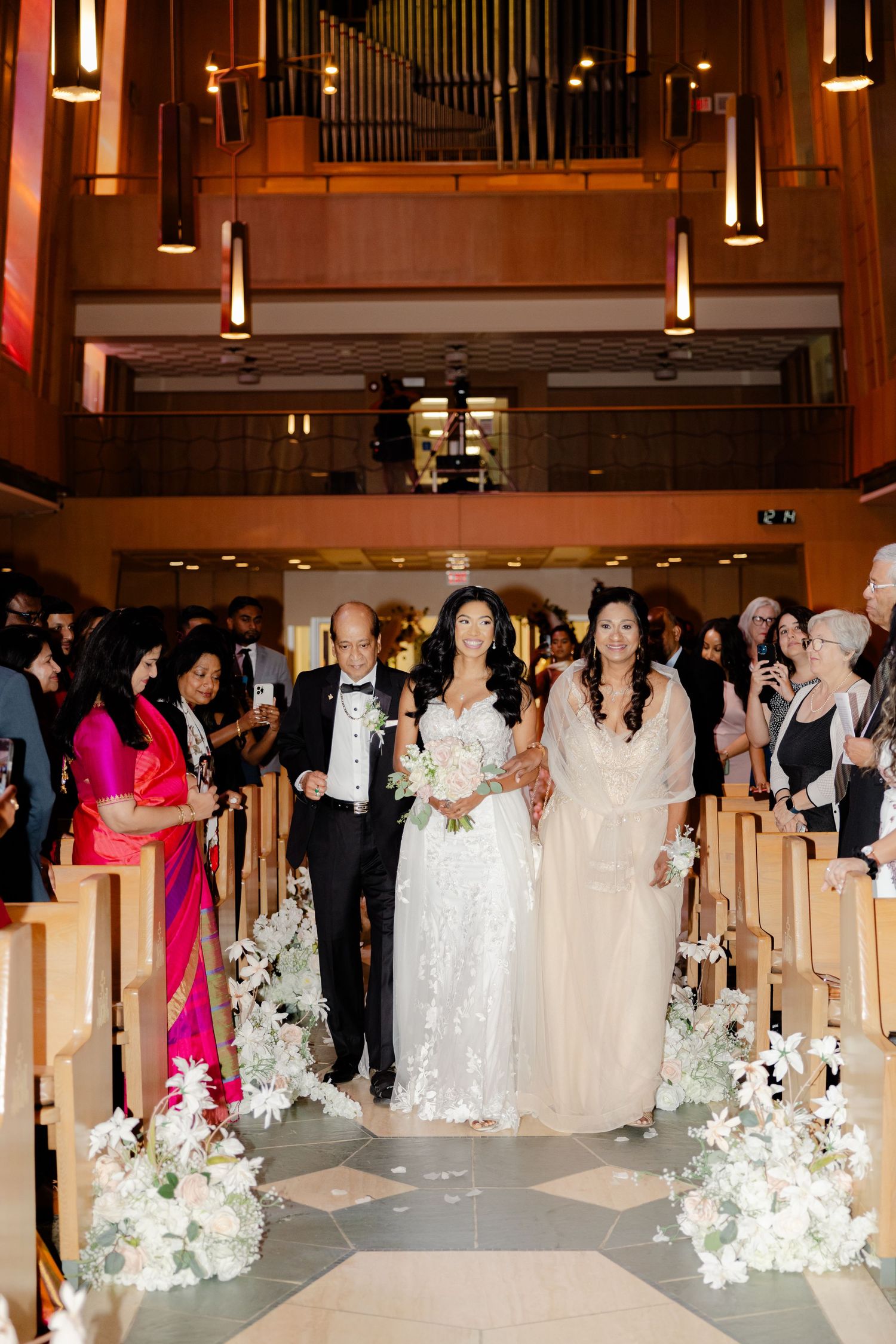 Wedding processional in church with traditional decor and floral aisle arrangements.