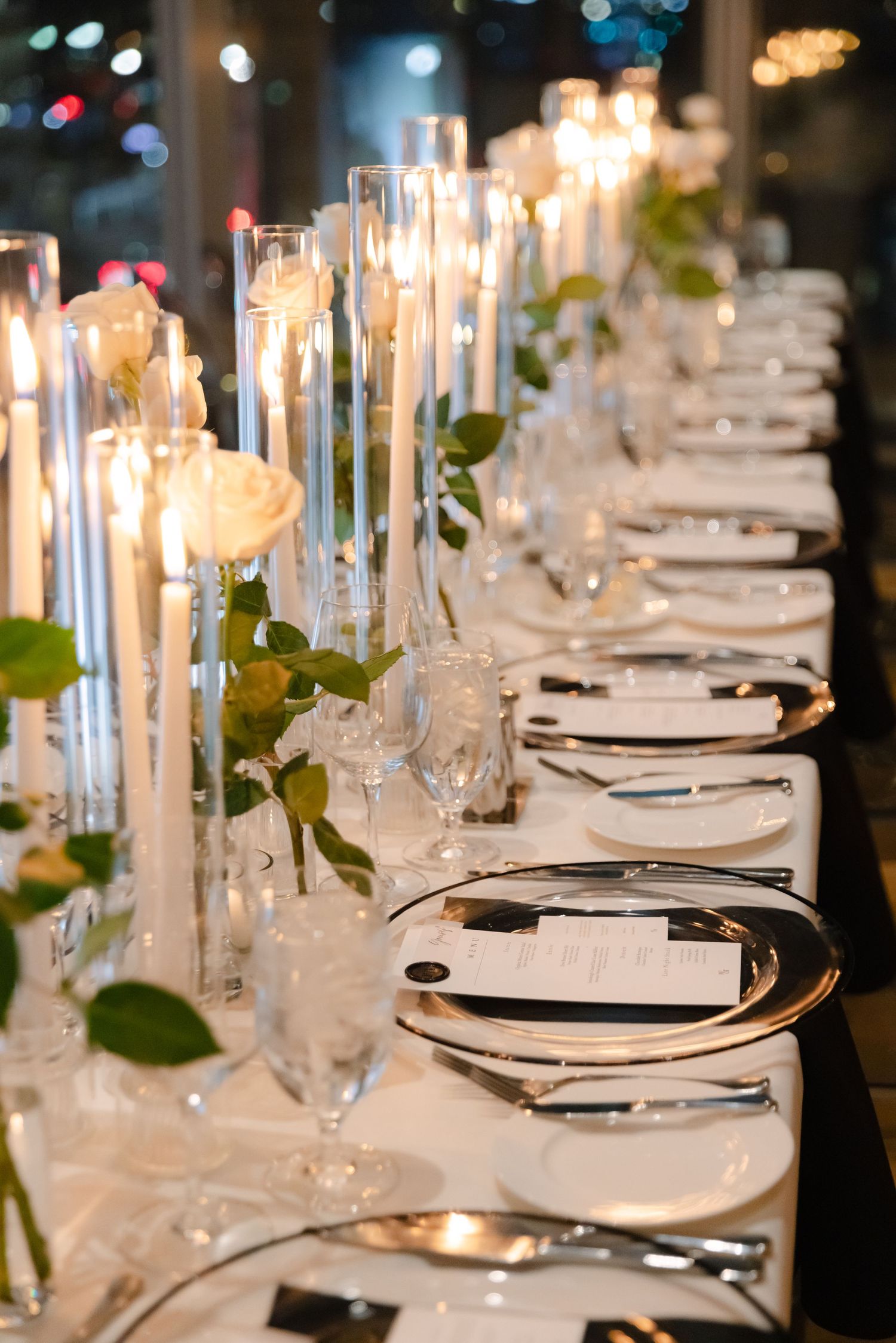 Luxurious table setting with tall candles, white roses, and crystal glassware for an elegant reception.