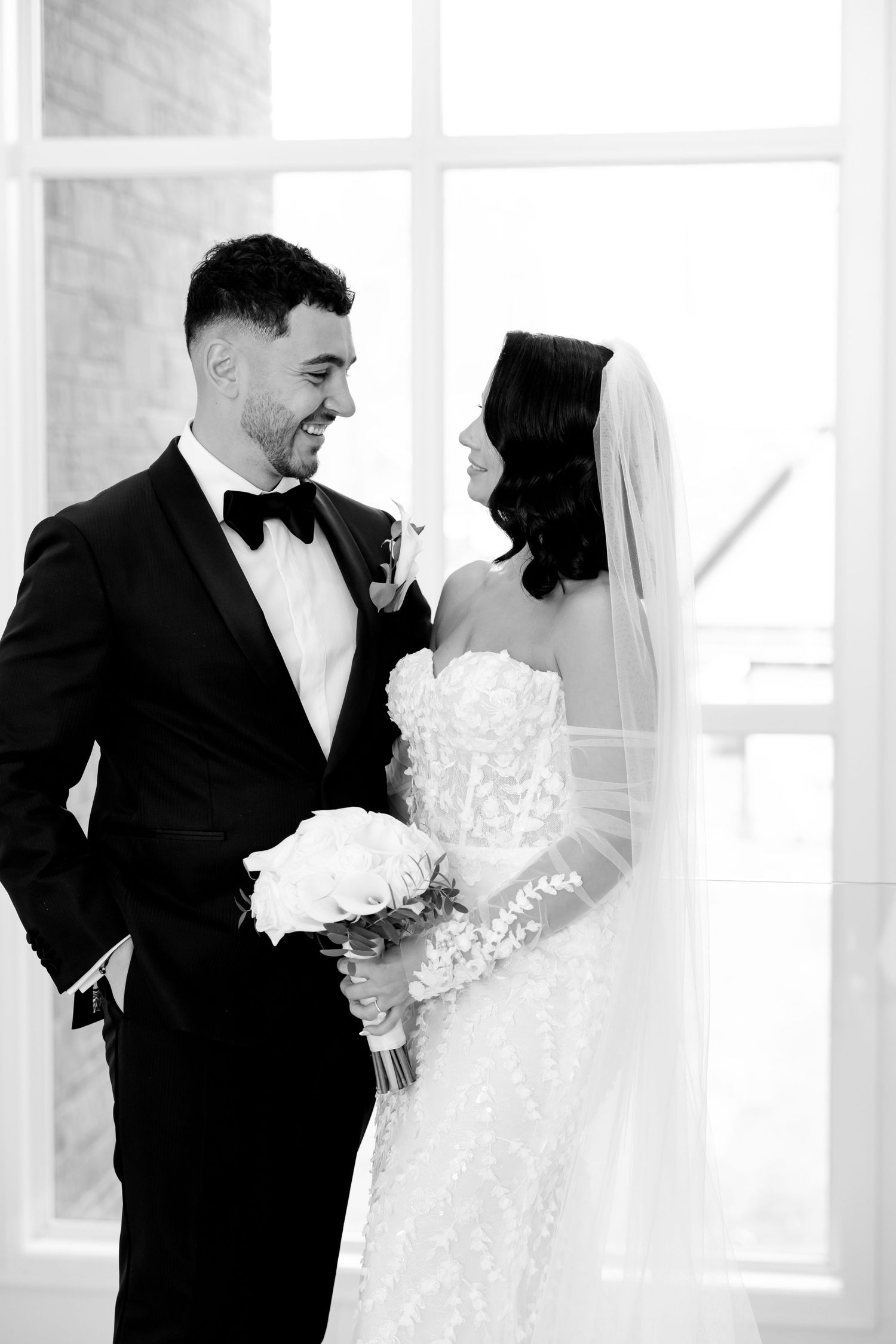 Black and white portrait of newlyweds sharing an intimate moment while holding white bouquet.