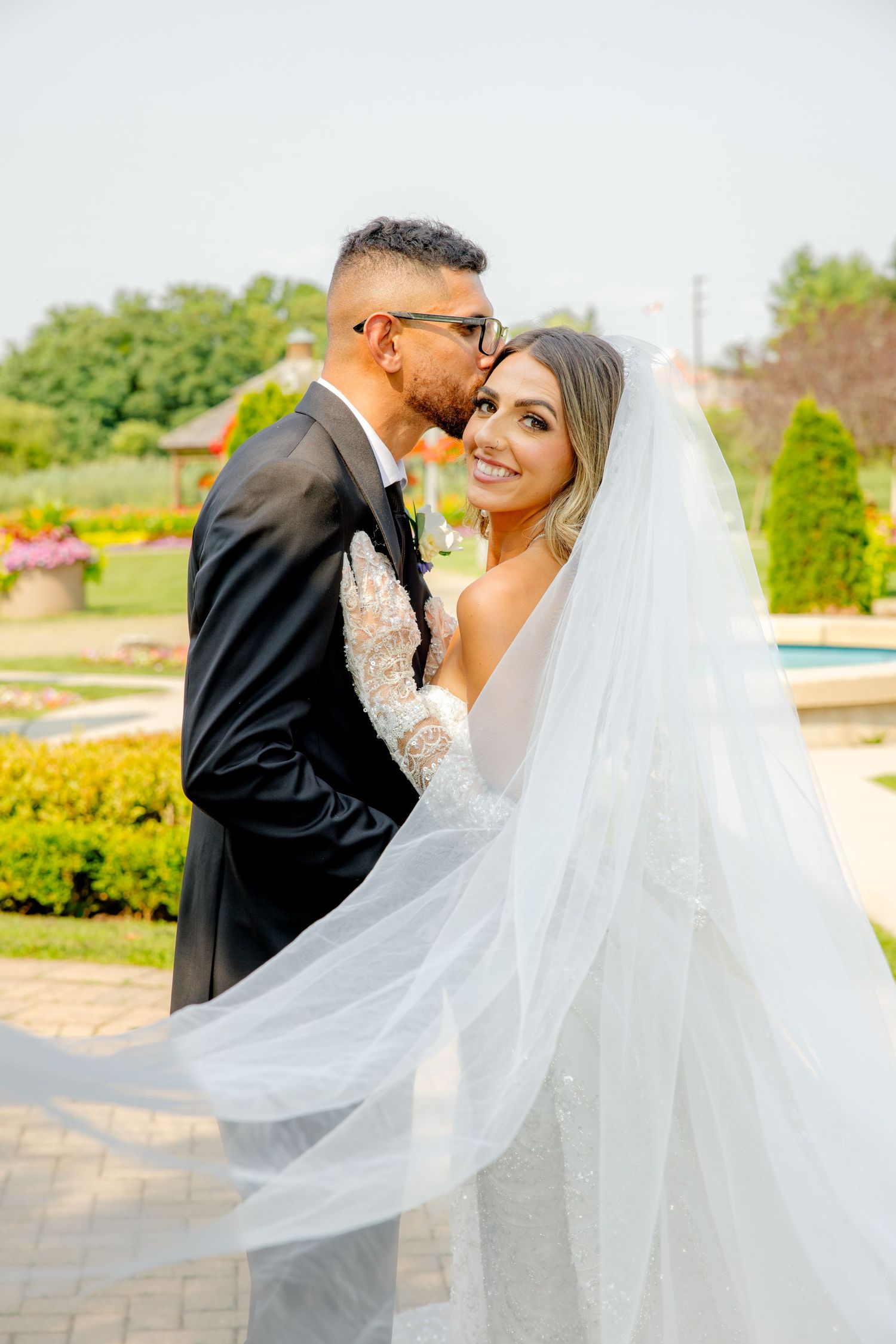 Intimate wedding portrait shows tender moment among landscaped gardens and flowing veil.