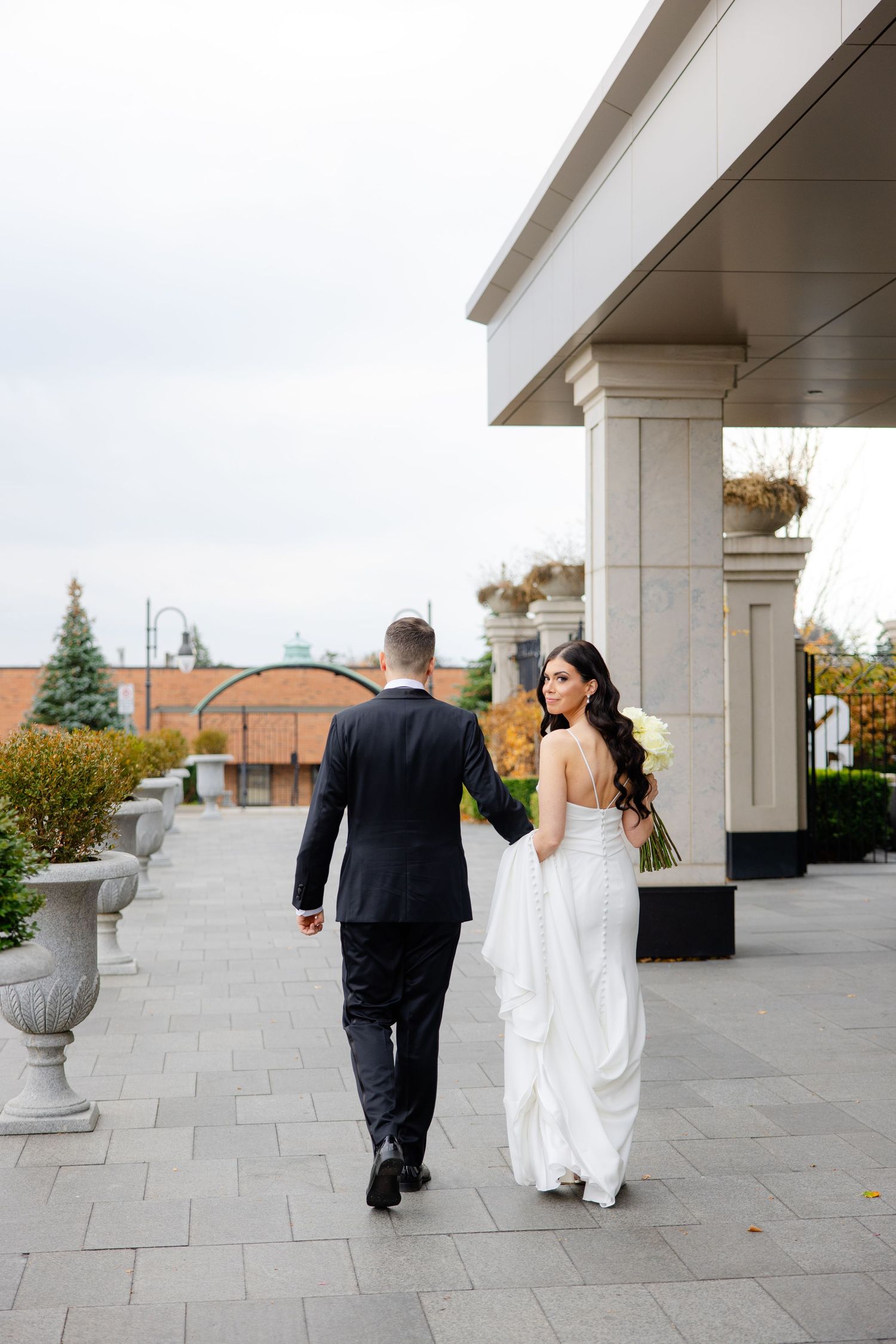 A bride and groom walk hand in hand along an ornate covered walkway.