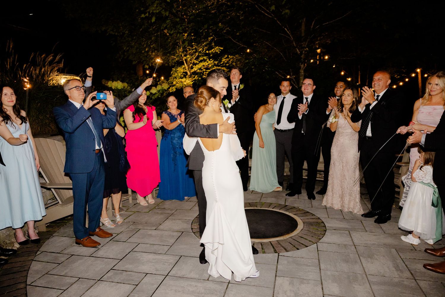 Guests cheer and celebrate as newlyweds dance during their outdoor evening reception.