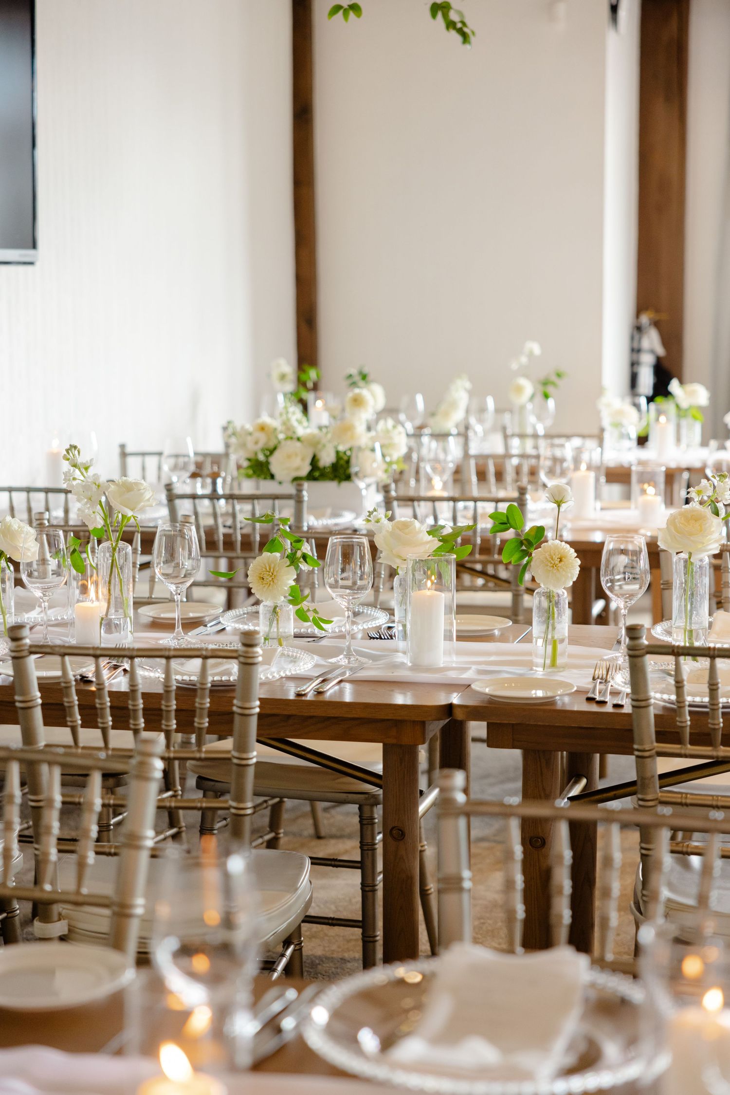 Wedding reception setup with wooden chiavari chairs, candlelit tables, and white floral arrangements.