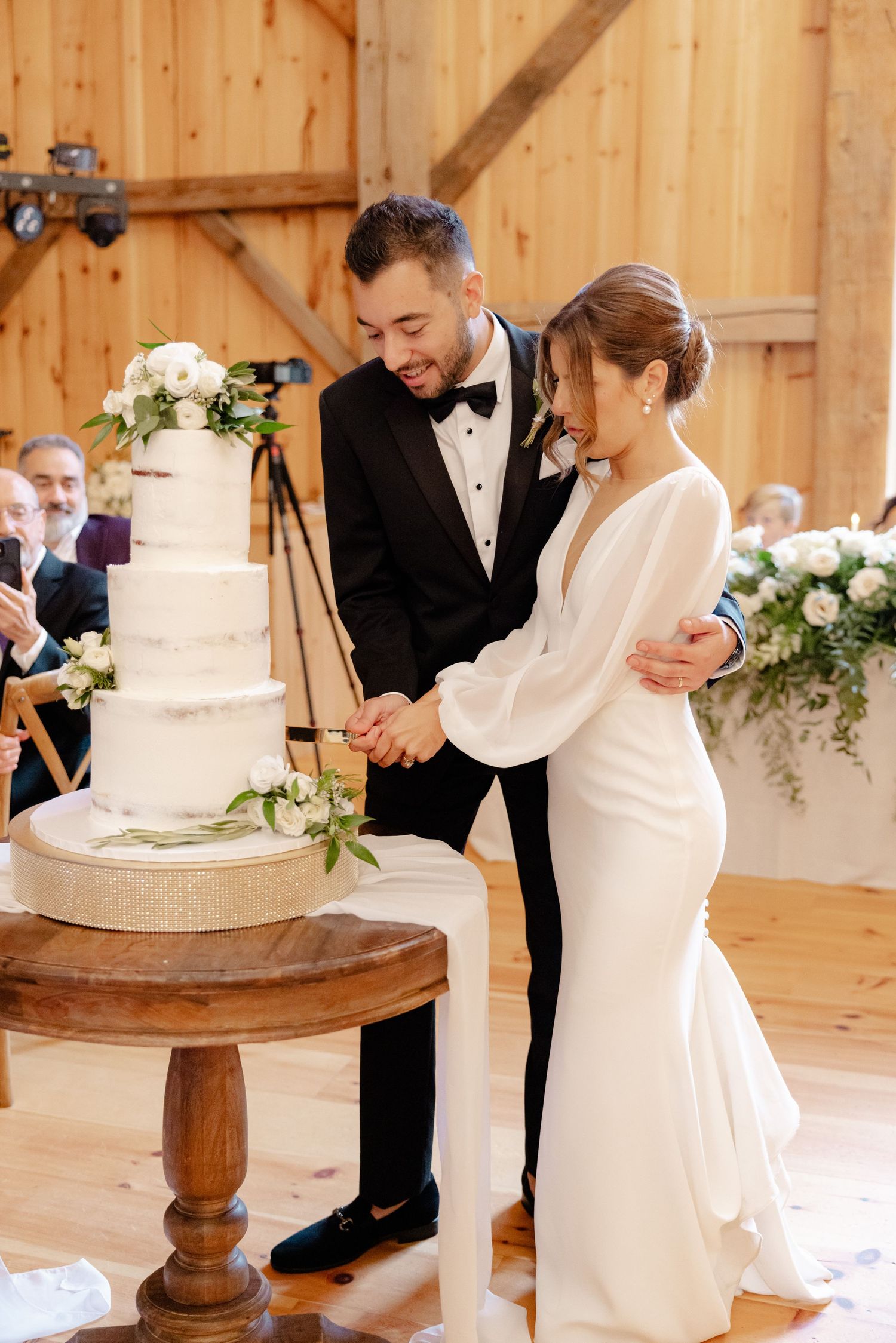 A couple preparing to cut their wedding cake in an elegant barn venue with wooden details.
