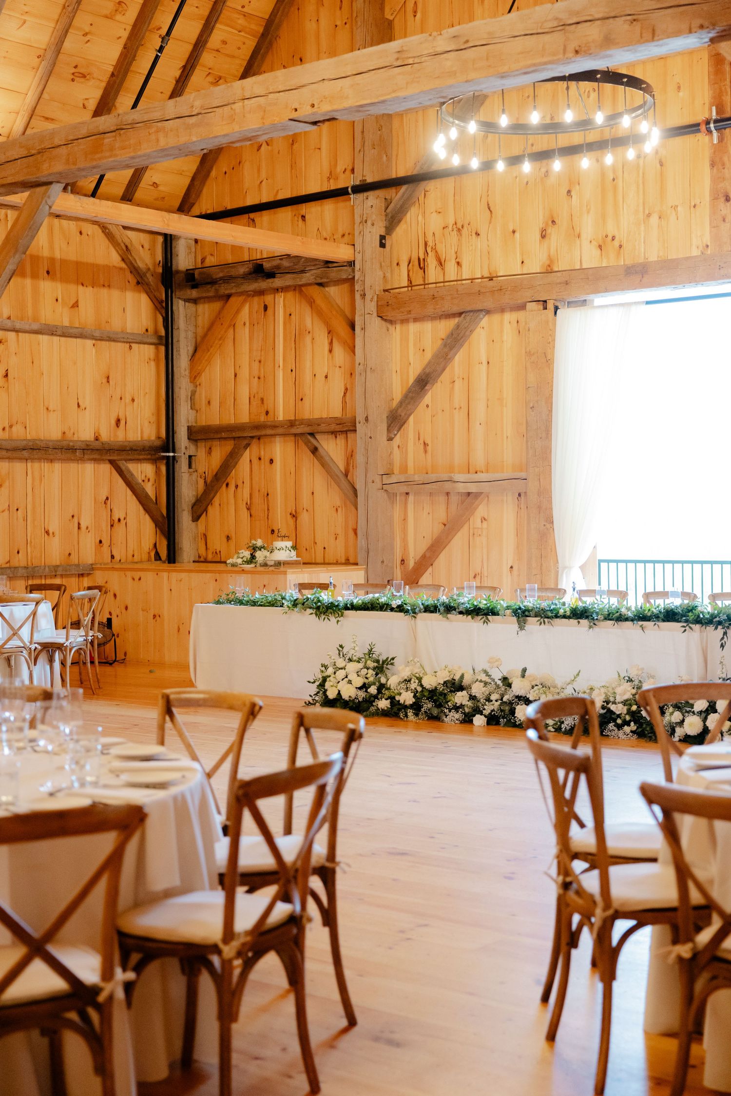 Rustic barn wedding venue with chandelier lighting and elegant white floral head table display.