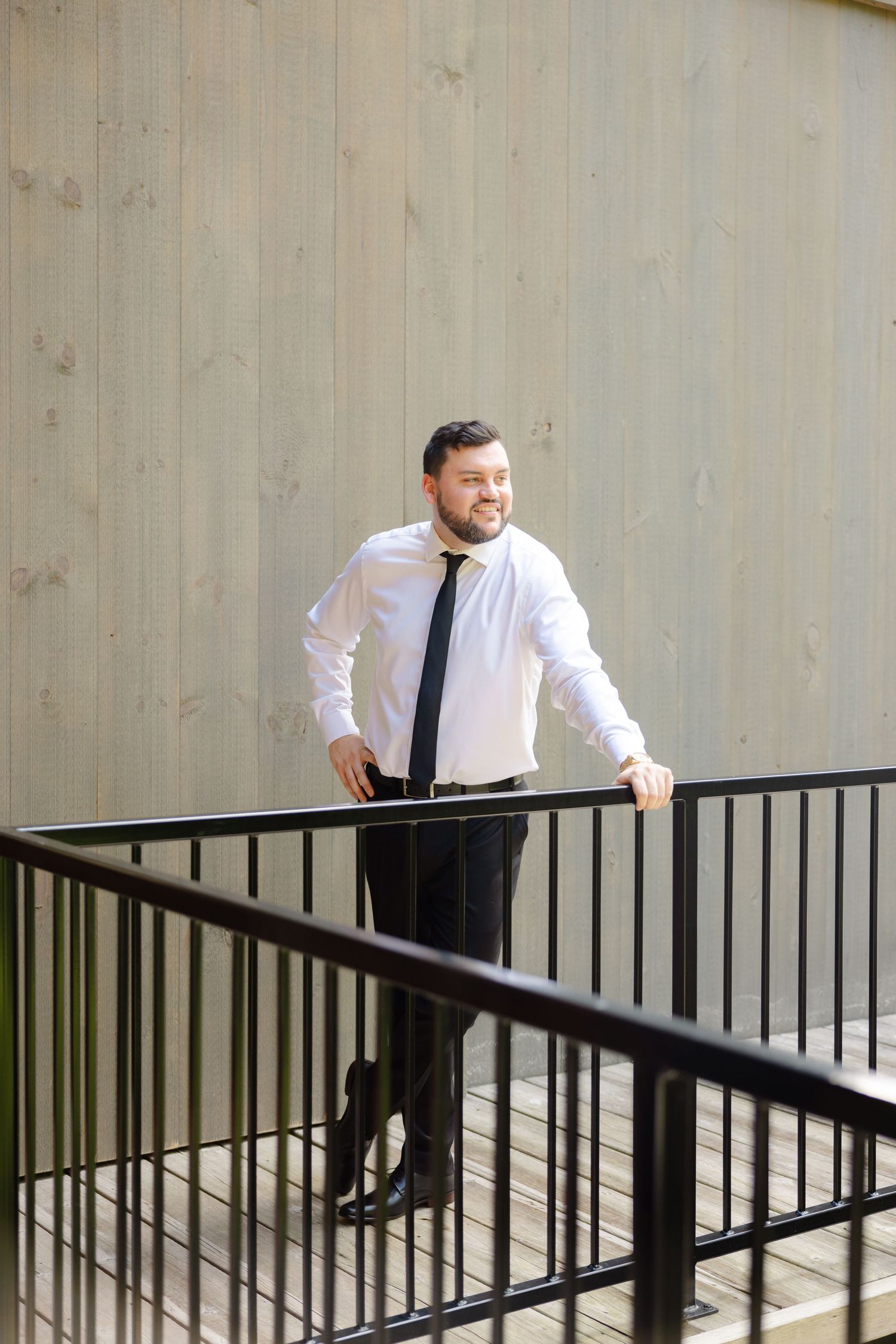 Person in business attire smiling while standing on outdoor deck with railing.